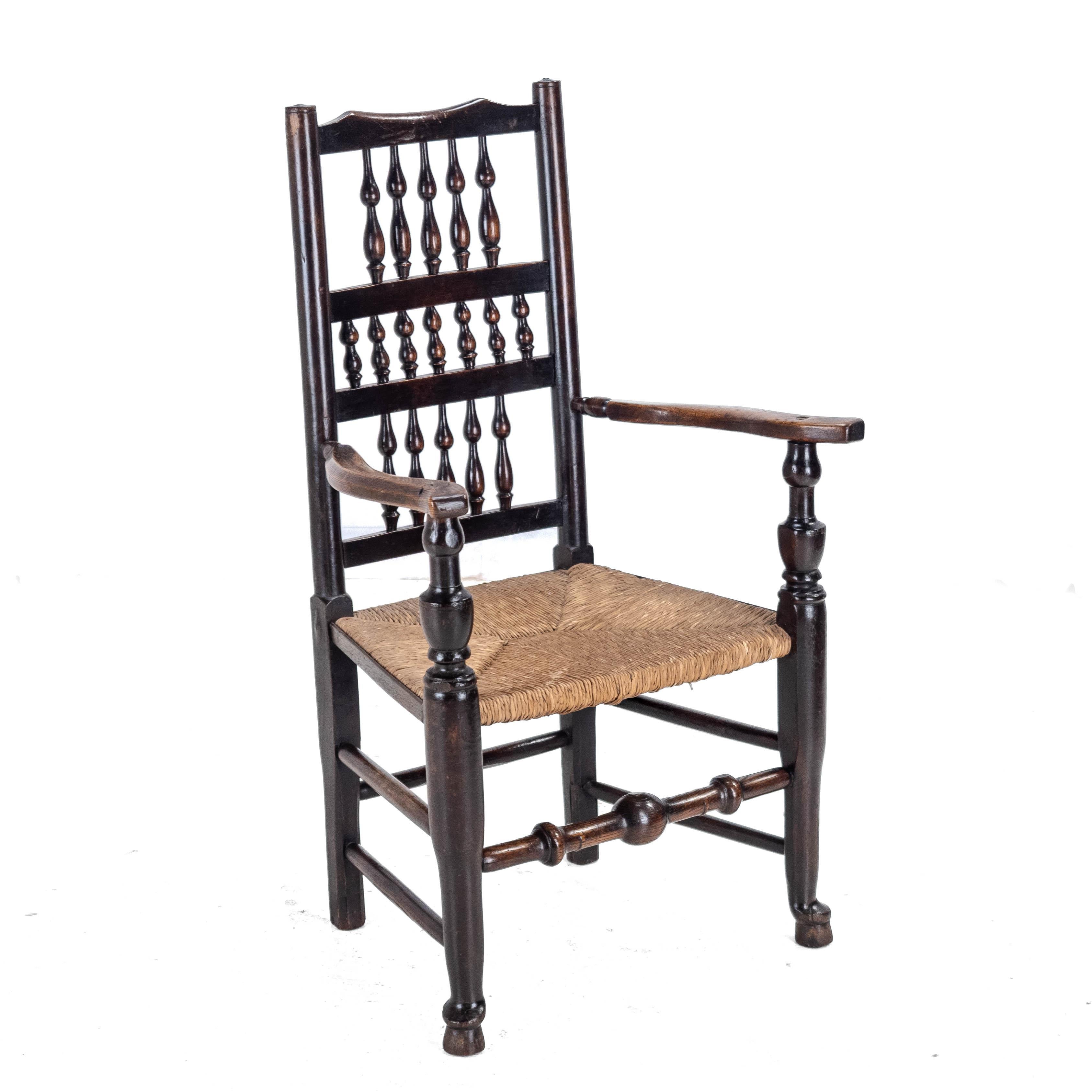 Sillón de tallista rural del siglo XIX, con armazón de olmo y fresno y asiento de junco, tipo Lancashire. Esta silla presenta un respaldo de tres filas de husillos torneados, montantes de estilo torneado, brazos abiertos con soportes torneados,