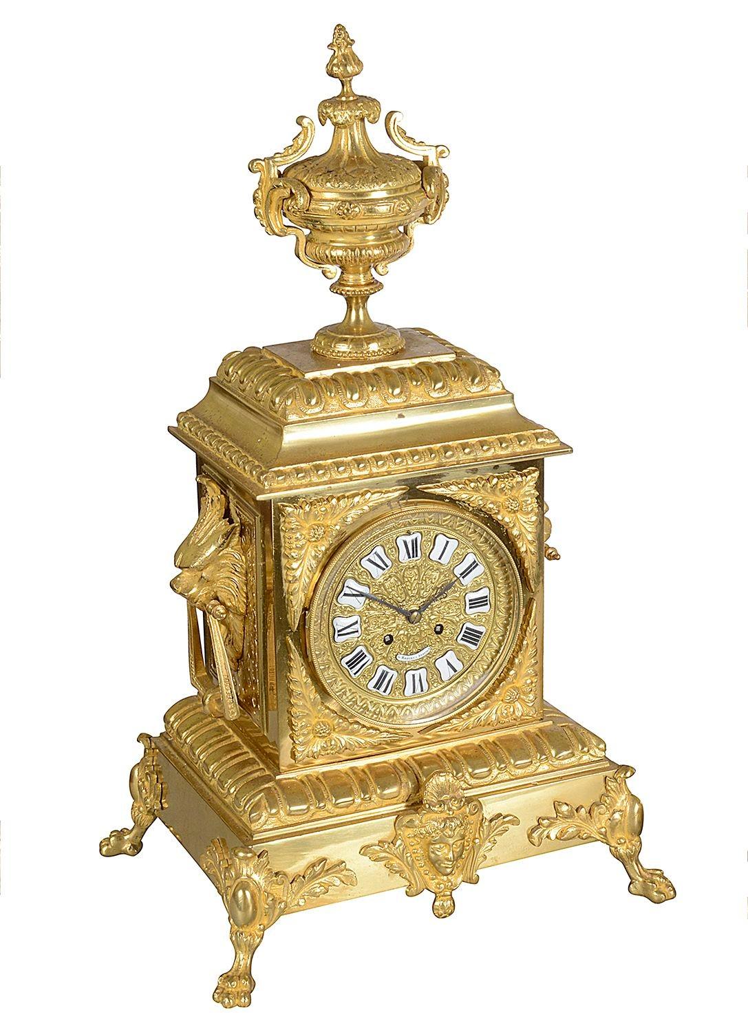 A French late 19th Century Louis XVI style gilded ormolu clock set. The clock having a classical urn mounted to the top, Lion mask drop handles either side of the clock, white enamel Roman numerals, an eight day duration movement, striking on the