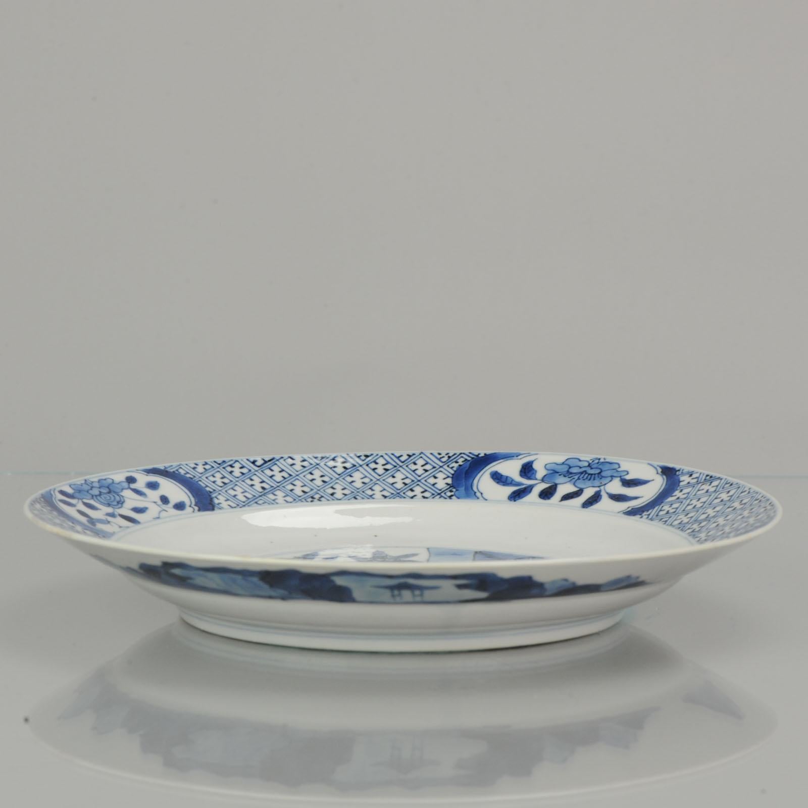 A blue and white plate decorated with a central scene of two elegant ladies in a courtyard, the border with four panels of flowers between swastika shading. Marked to the back with the six character mark for Wanli within a double circle. The mark to