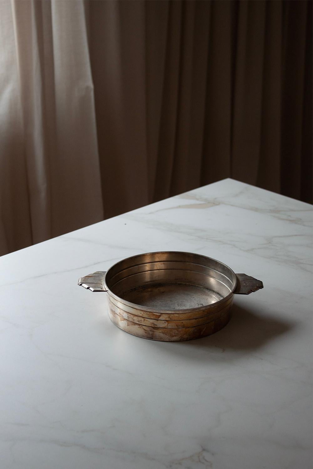 Looking back at the 1920s this little silver plated vessel is a wonderful representation of the art deco period. This silver plated bowl or plater is decorated with strong shapes at the Handels, while the rest is keep minimal and simple. This art