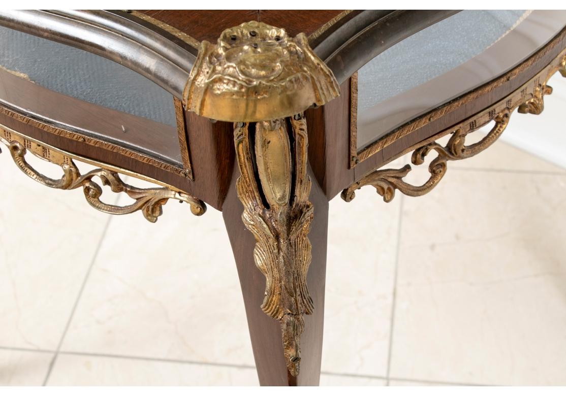 Fine jewel like Vitrine Table in Louis XV style. Shaped square form with hinged glass inset top and glass sides. The inside lined in a dusty blue herringbone fabric. The top with brass trim and gilt brass cartouches on the corners. The apron with
