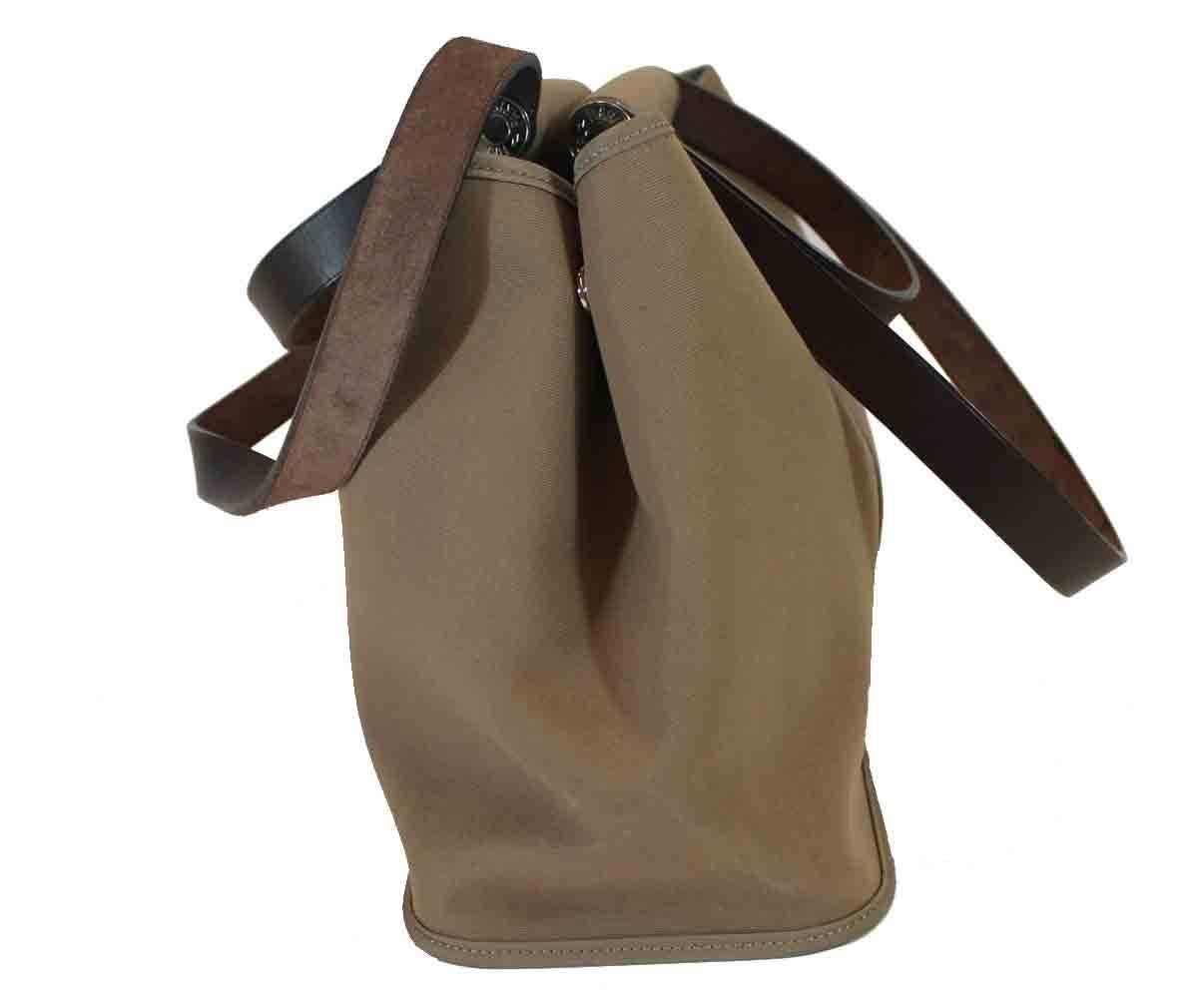 Taupe canvas. Brown leather trim. Palladium hardware. Flat shoulder straps and top handles. One open interior pocket. One interior zippered pocket.