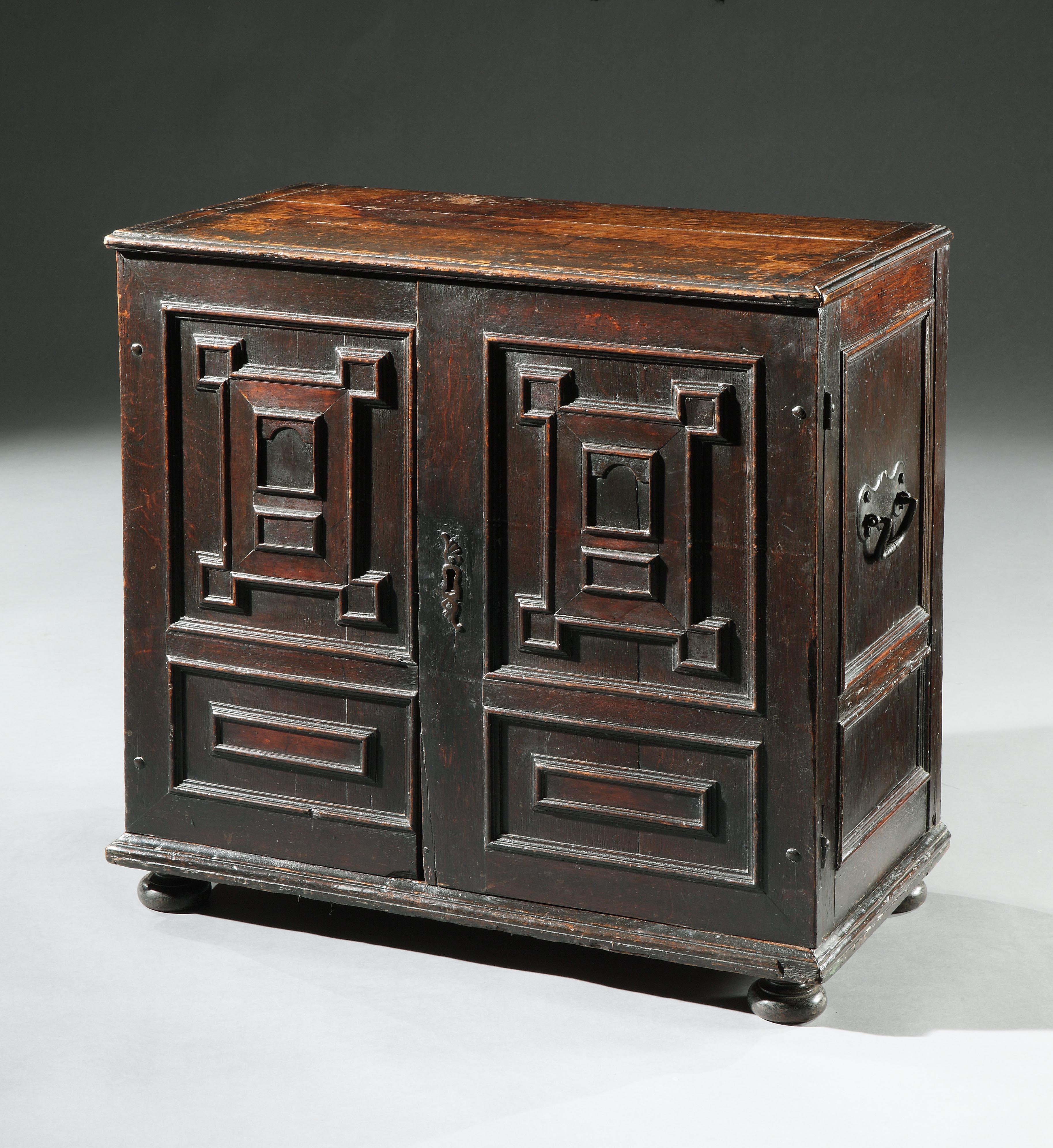 A late 17th century, oak cabinet with a fitted, teak interior enclosing secret drawers

The plank top in two sections, cleated and faced with a moulded edge. The cupboard with two doors decorated with applied, geometric mouldings. The hinges