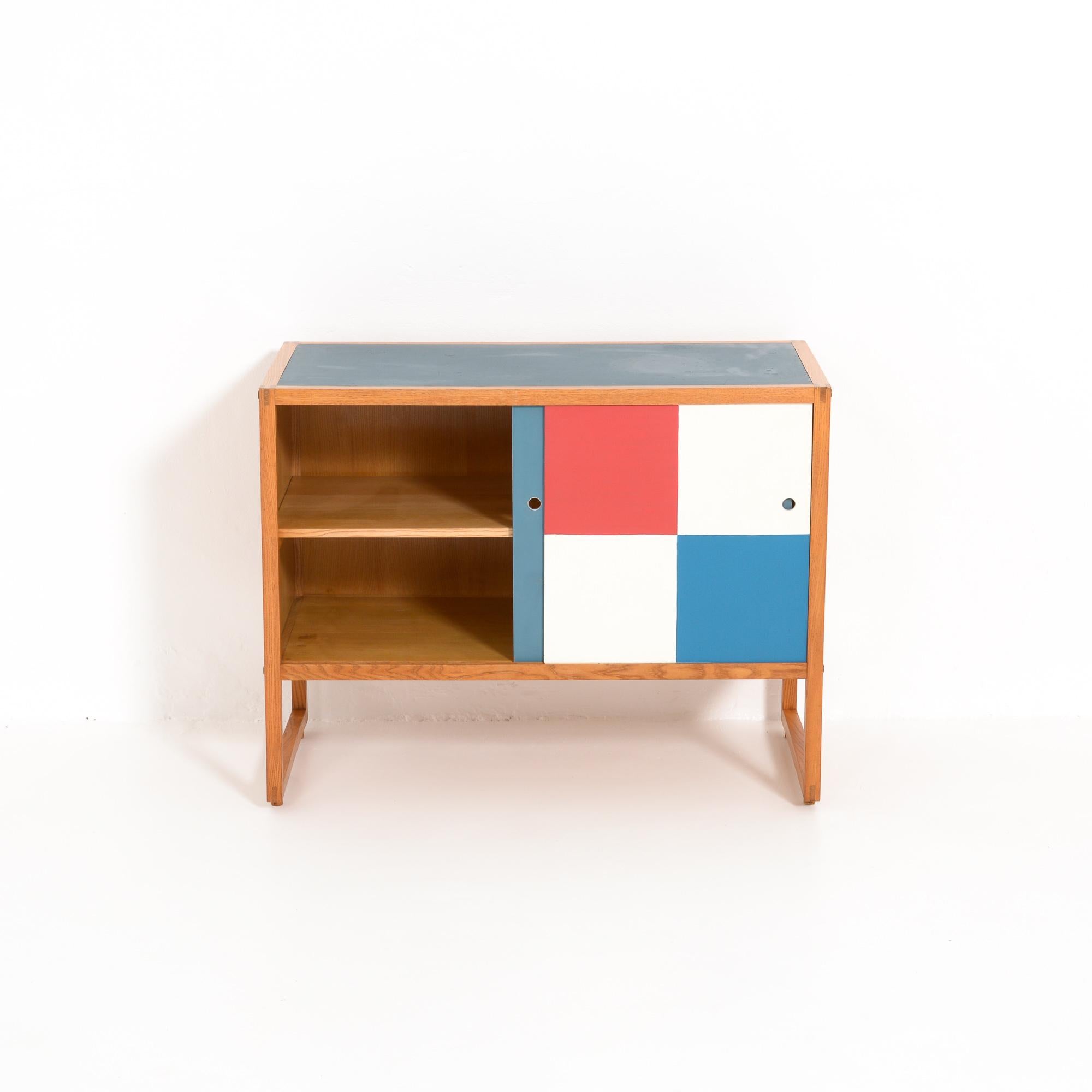 This cabinet was designed by Pieter De Bruyne in 1957 and manufactured in 1958.
Characteristic of De Bruyne’s work is the pure design with an eye for detail.
This cabinet is made of ash wood with a blue linoleum top. The two colorful sliding doors