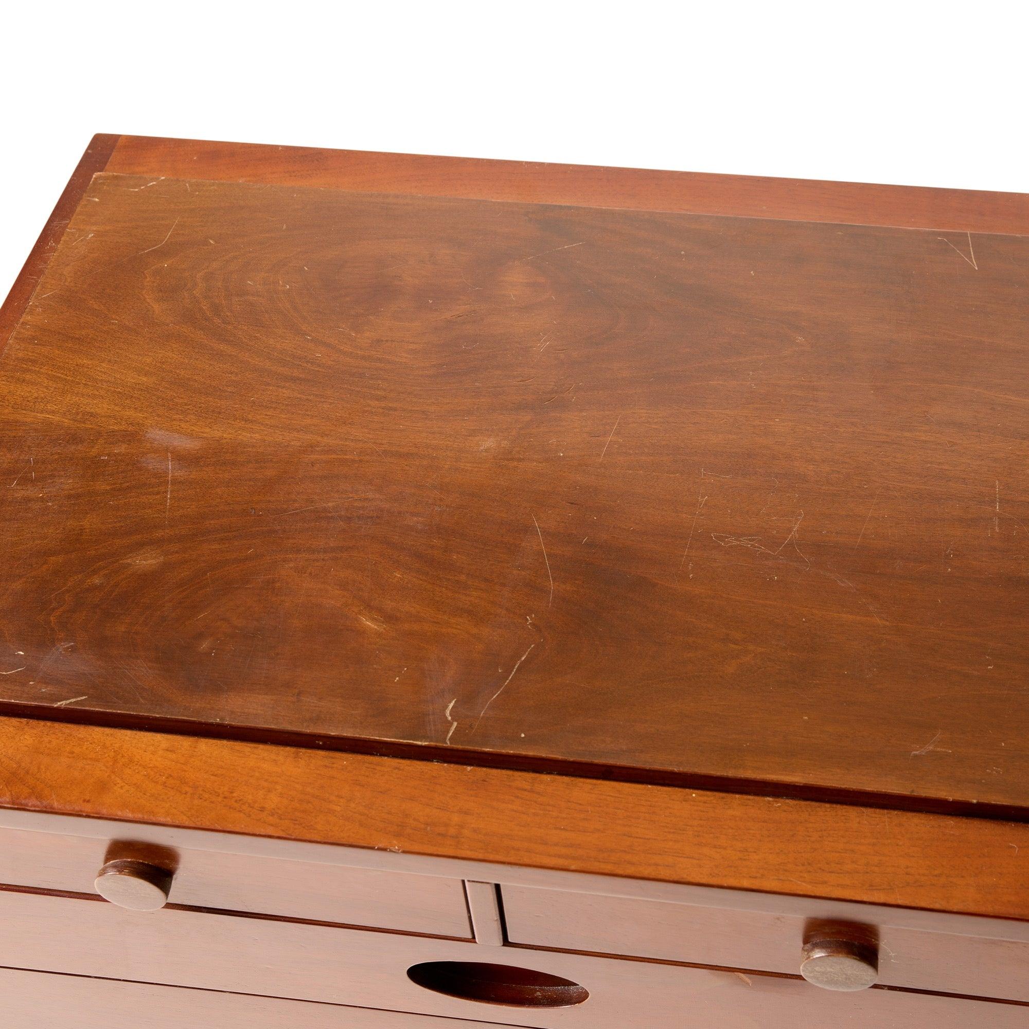 A walnut cabinet with two (2) top drawers having oval handles and three (3) drawers with oval integral handles, on cylindrical legs with satin aluminum stretchers. Cabinet is topped with a slightly raised removable / reversible board.