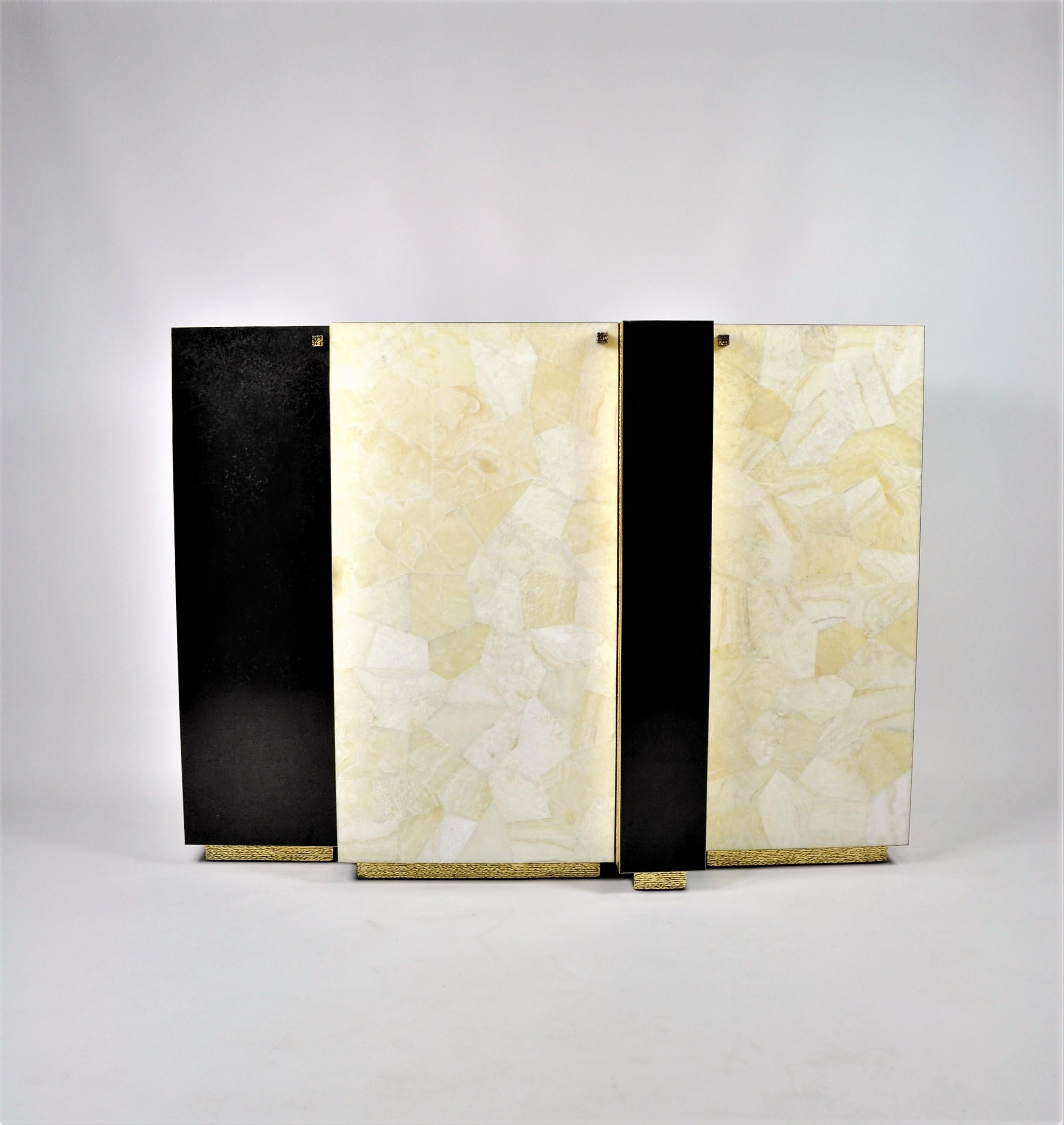 This unique cabinet has three doors and it is made of various marquetries with brass trims.
The sides and the top are in natural fiber marquetry covered with gold leaf.
The white doors are in rock crystal whereas the black doors are in granit