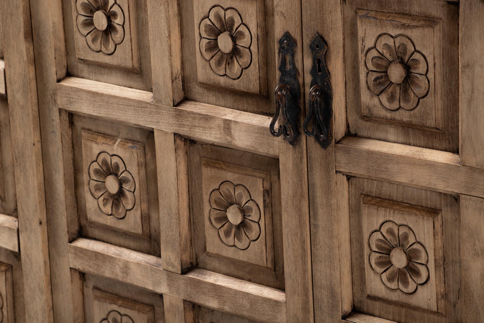 Una fachada de rítmicas flores emerge de un campo de tranquila geometría: cada rosetón está delicadamente encastrado en su propio nicho cuadrado, como exvotos colocados en el muro de una capilla. Este mueble no se presenta como un mueble, sino como