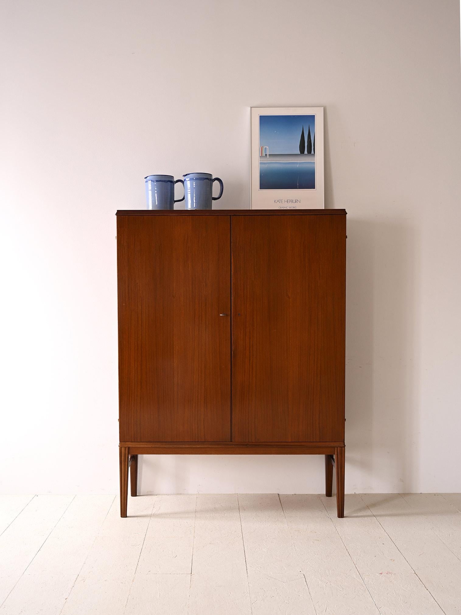 Vintage cabinet with hinged doors.

This elegant cabinet with regular lines features two lockable hinged doors and long tapered legs that slender the figure.
Internally it is divided into compartments made of shelves and small drawers.
Suitable as