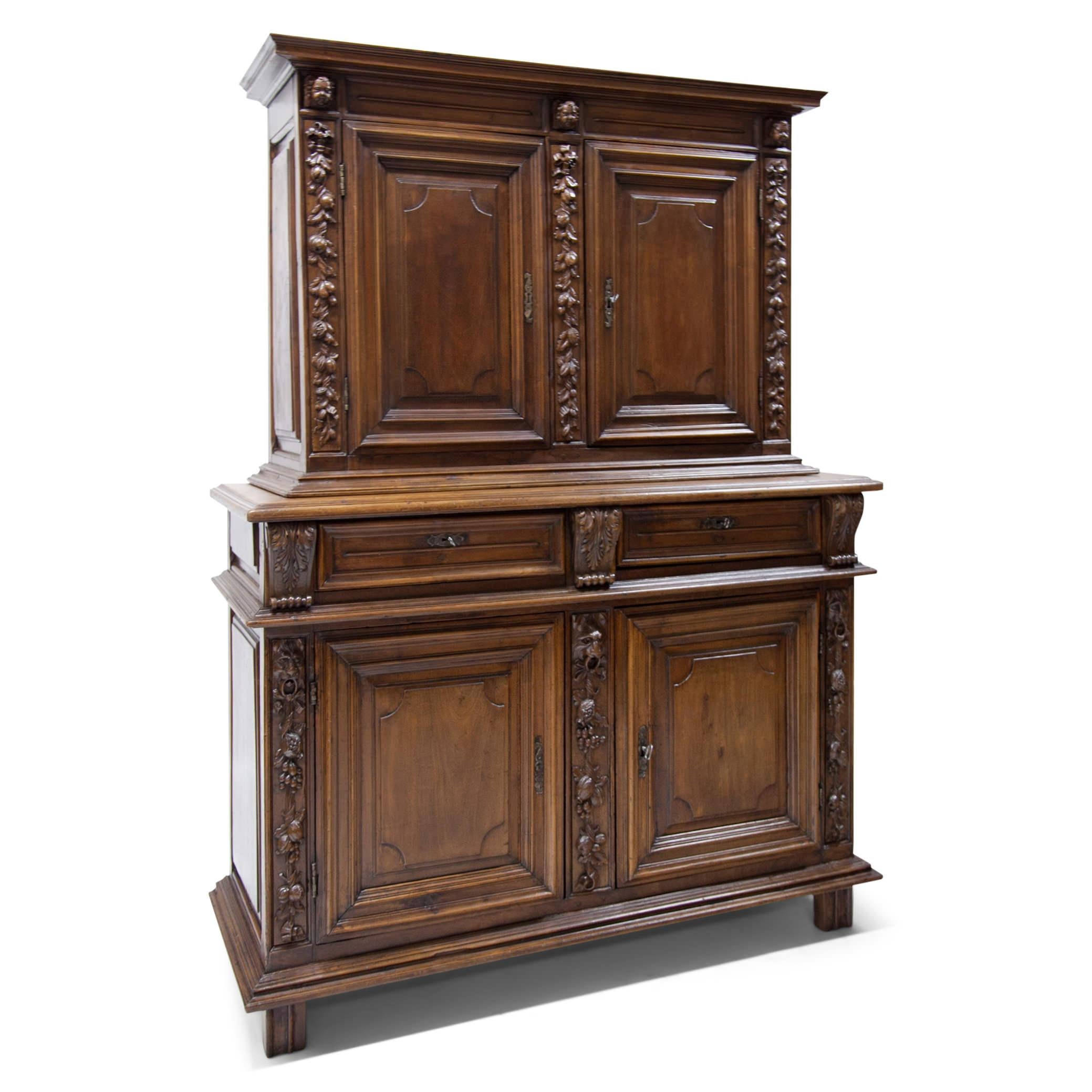 Cabinet à deux corps made out of stained walnut. The two-door base is on pad feet, the doors show fillings and moldings, the pilasters are decorated with carved fruit decor and lion head mascarons. This is followed by two drawers with volute