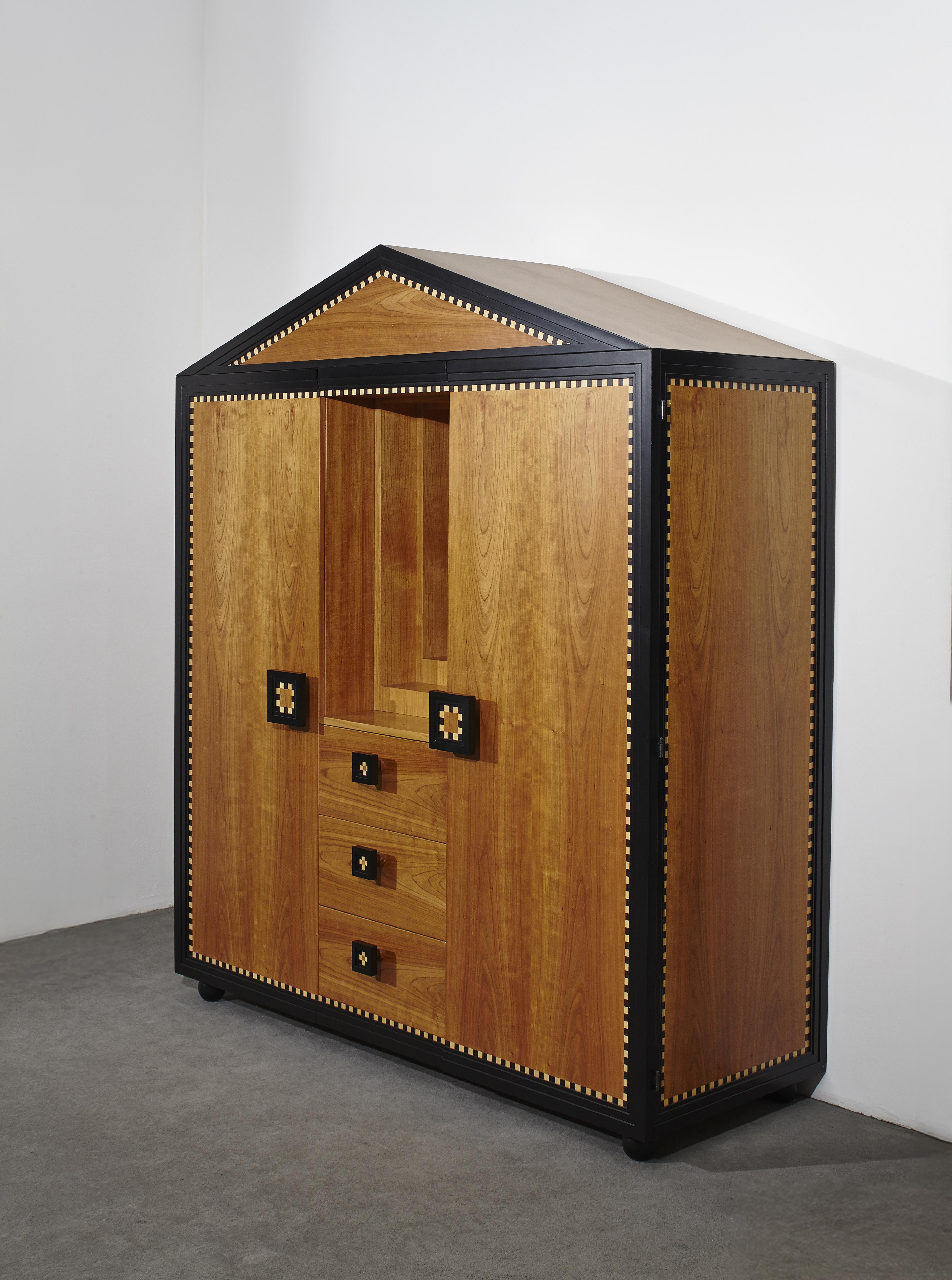 Mobile progettato da Paolo Portoghesi per Meccani Arredamenti nel 1980. Il mobile è dotato di tre cassetti centrali che dividono le due ante laterali e di uno specchio incorporato. Sotto allo specchio è presente una scala di strati in legno, che