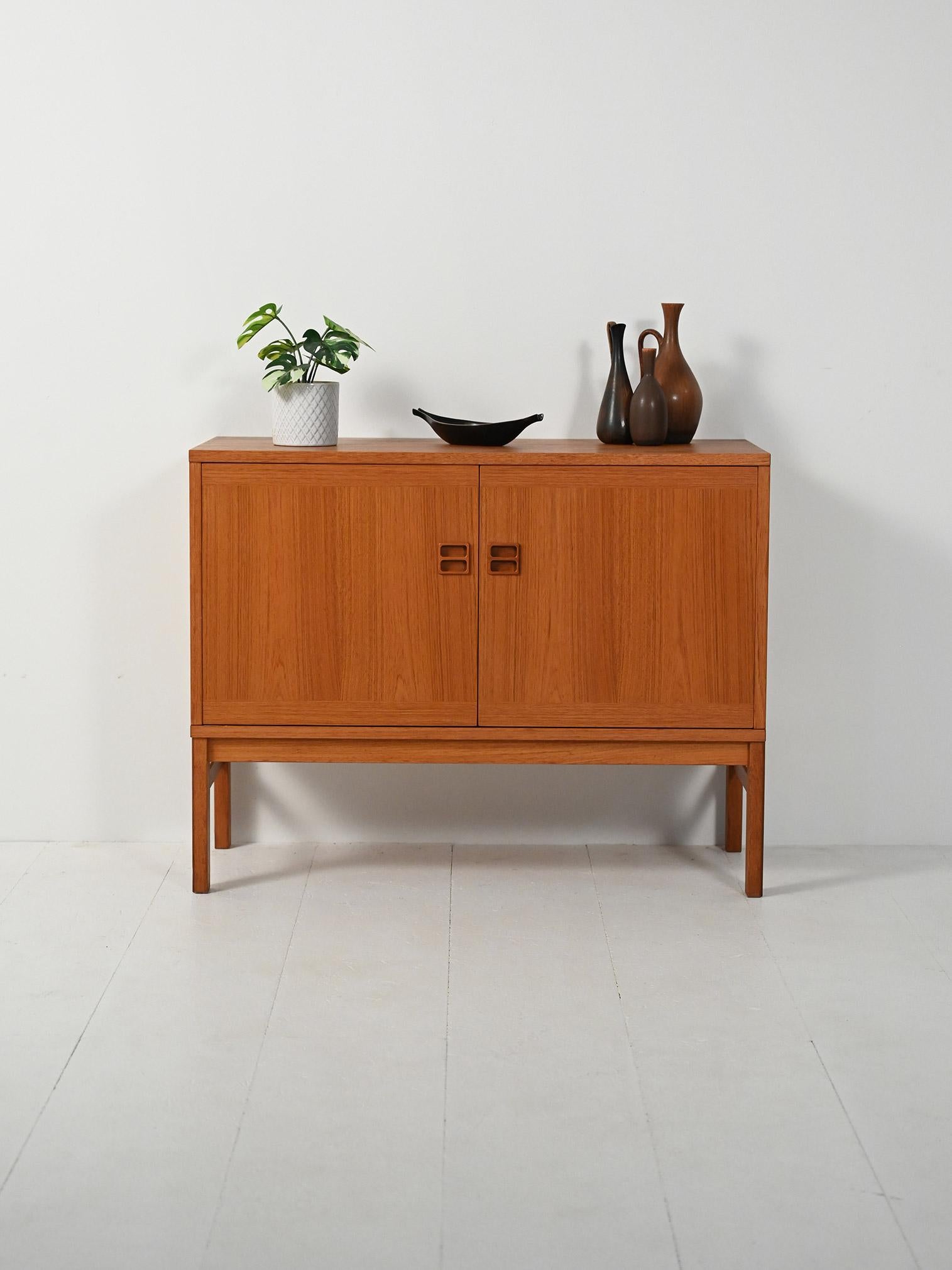 Cabinet in teak con due ante a battente, maniglie intagliate a doppia foratura e linee geometriche che valorizzano la venatura del legno.

Elegante cabinet scandinavo in teak, anni ’60, impostato su basi leggere e volumi rigorosi. Le due ante a