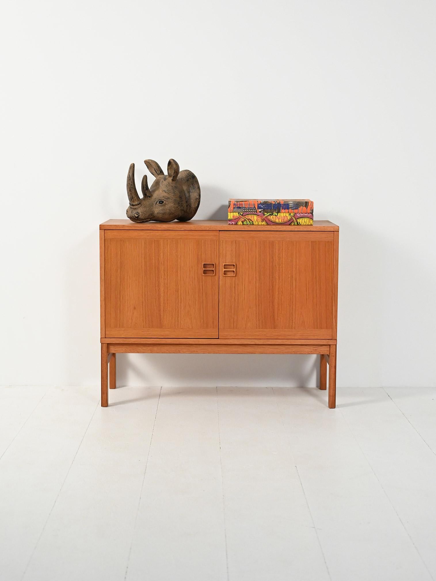 Cabinet in teak con due ante a battente, maniglie intagliate a doppia foratura e linee geometriche che valorizzano la venatura del legno.

Elegante cabinet scandinavo in teak, anni ’60, impostato su basi leggere e volumi rigorosi. Le due ante a