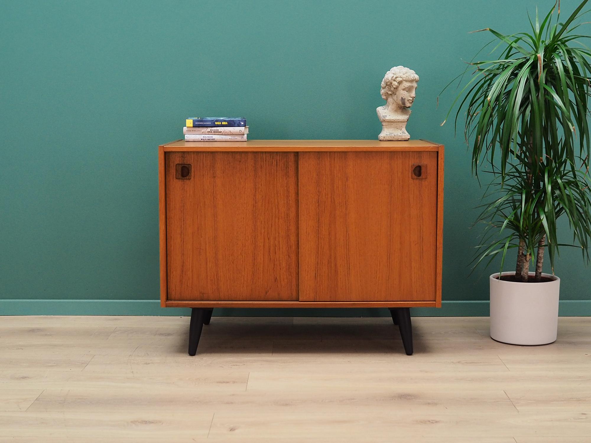 Brilliant 1960s-1970s teak cabinet, Minimalist form, Danish design. The furniture is covered with teak veneer, legs are made of solid wood. The furniture has two sliding doors, behind which there is one shelf. Preserved in good condition (small