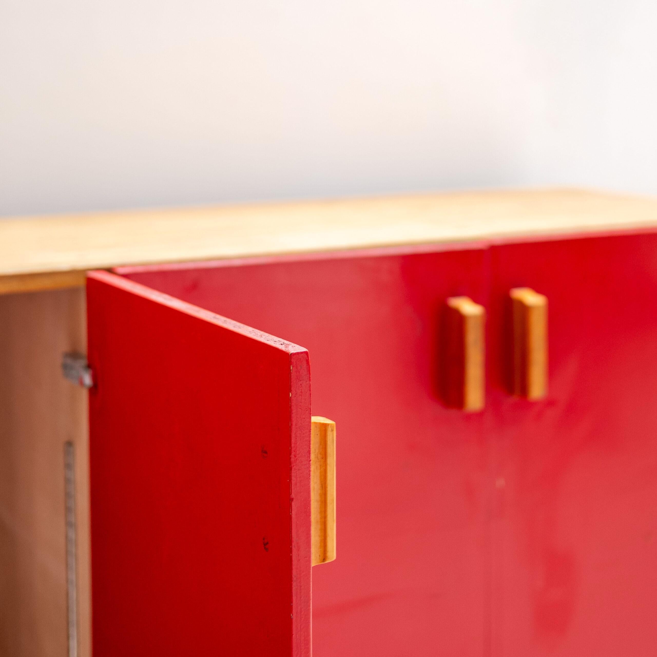 Armoire en bois de Charlotte Perriand, avec des portes rouges frappantes et un cadre en pin massif. Ses lignes pures et son contraste naturel incarnent le signe du design de Perriand - fonctionnel, chaleureux et intemporel.