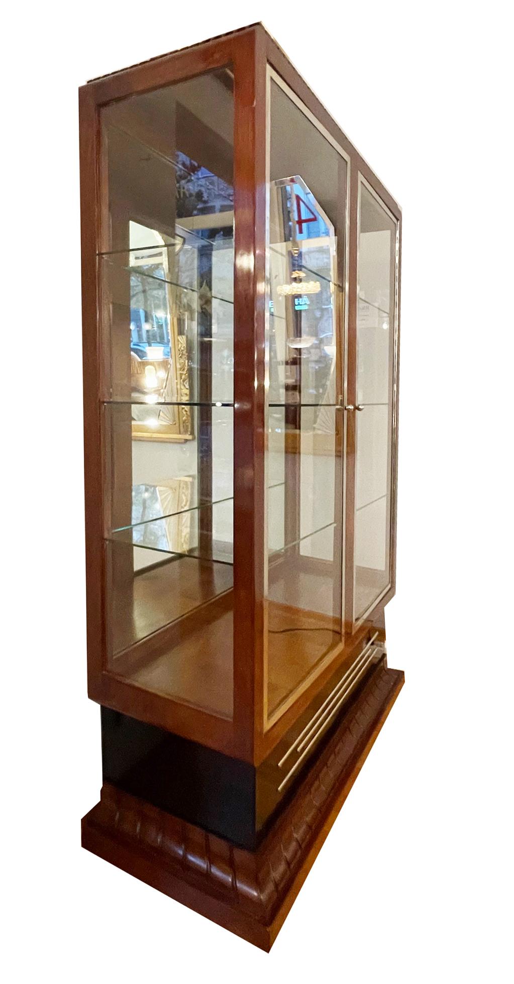 Art Deco display cabinet with three sides glazed
France around 1930.

Rosewood veneer, black lacquer base with chrome strips.

Two-door glass doors framed by nickel-plated metal frames.

Compartment dividers with 3 glass shelves.

Mirrored back