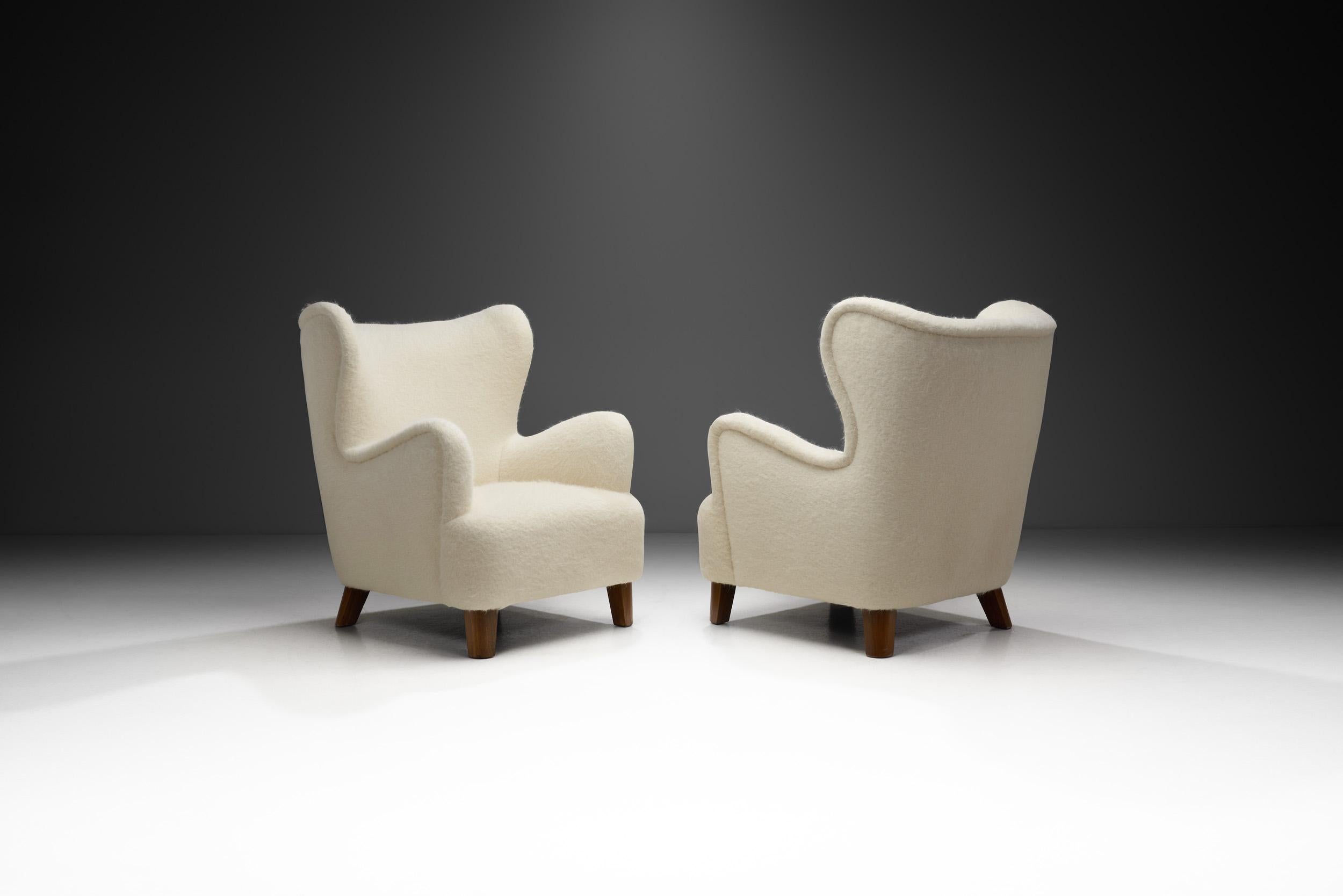 This elegant pair of winged back chairs is a great representation of the quality and craftsmanship of European master cabinetmakers of the 20th century and the immediately recognizable characteristics of the era’s design. With the organically curved