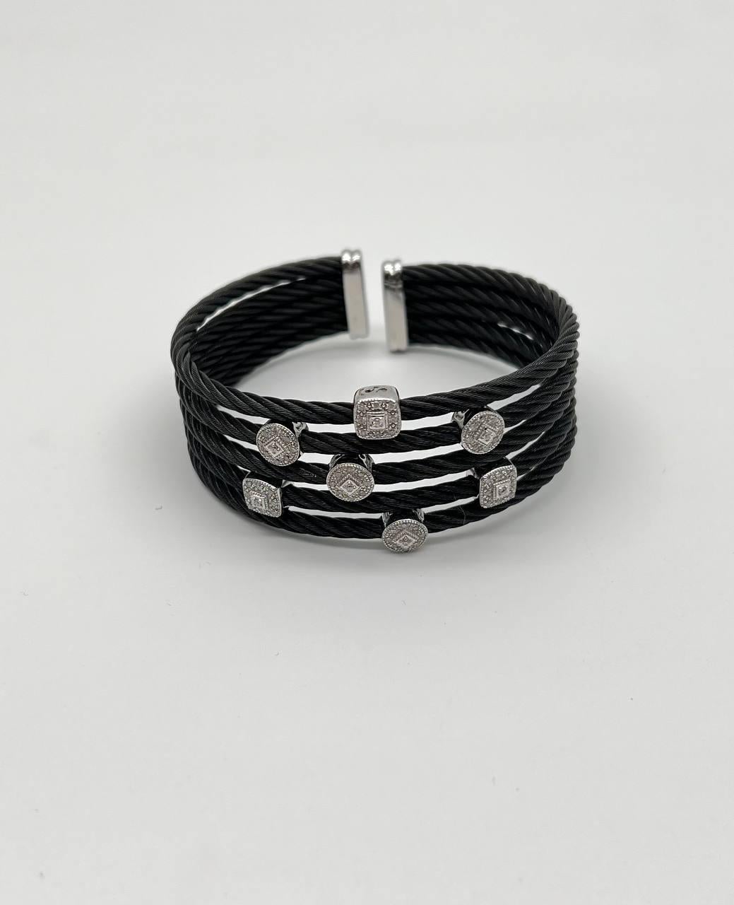 Un braccialetto moderno con più fili di cavi neri e acciaio intrecciati. Il design è impreziosito da diamanti rotondi in cesti quadrati, che aggiungono un tocco di brillantezza.
Lo stile aperto del polsino consente di indossarlo e regolarlo