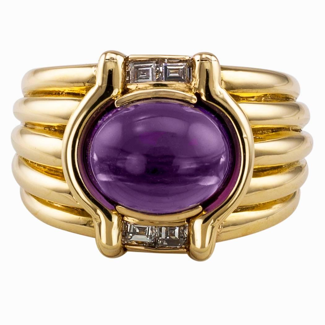 Cabochon amethyst and diamond gold ring band circa 1990. The wide fluted design centers upon an oval cabochon amethyst set within a parenthesis-shaped bezel, flanked, at the open ends of said parenthesis, by pairs of square-cut diamonds totaling