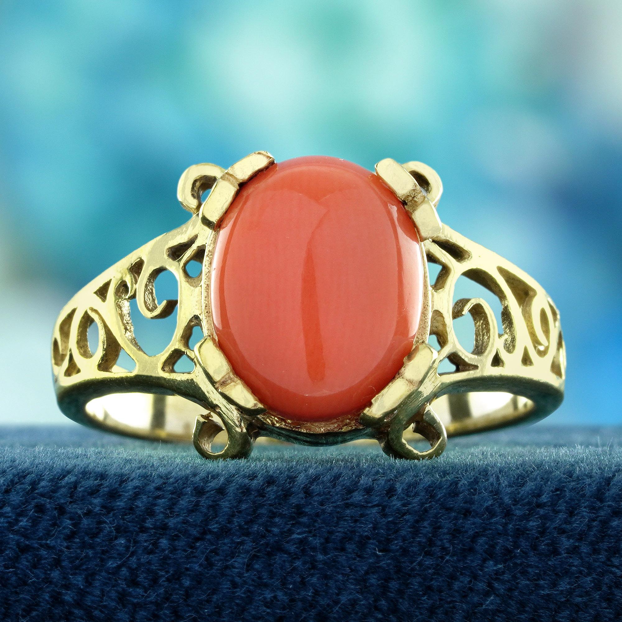 A masterpiece of elegance and timeless design. At its heart lies a smooth cabochon coral, celebrated for its rich, warm hue that symbolizes energy and passion. An intricate filigree band, showcasing delicate vintage-inspired patterns that add a