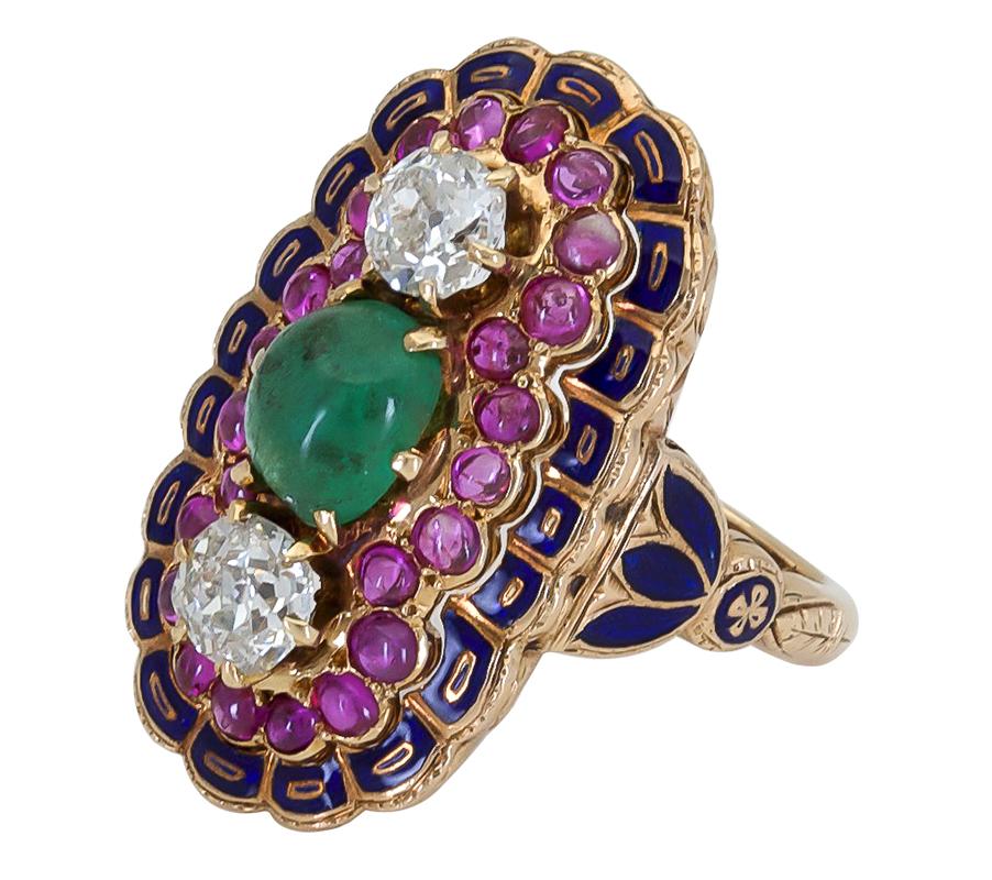 A unique and color-rich cocktail ring featuring a cabochon emerald center, accented by antique cut diamonds on the north and south of the stone. The three stones are surrounded by a row of ruby cut diamonds and finished with blue enamel accents in