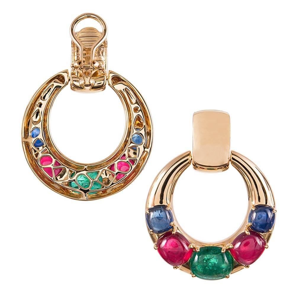 Graduated cabochons of blue sapphire, ruby and emerald are complimented by polished golden hoops and set in 18 karat yellow gold, compliments of iconic jewelry designer Seaman Schepps. The earrings measure 1.5 inches long and just under 1.25 inches