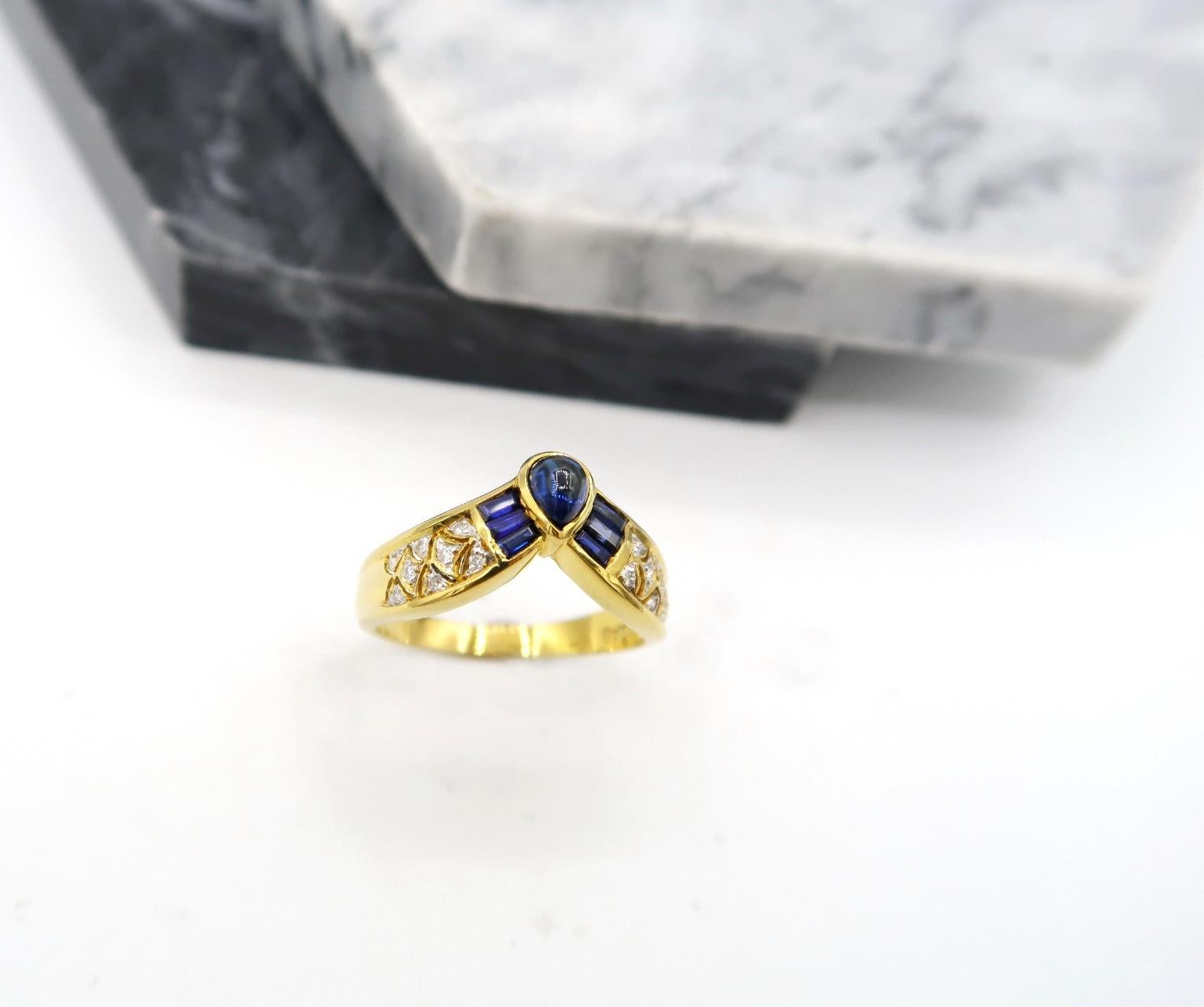 Cabochon Pear Shaped Blue Sapphire Chevron Wishbone Ring in 18K Yellow Gold embellished with channel set baguette blue sapphire and diamond lace scale detail

Ring size: 53.5
Please let us know should you wish to have the ring resized.