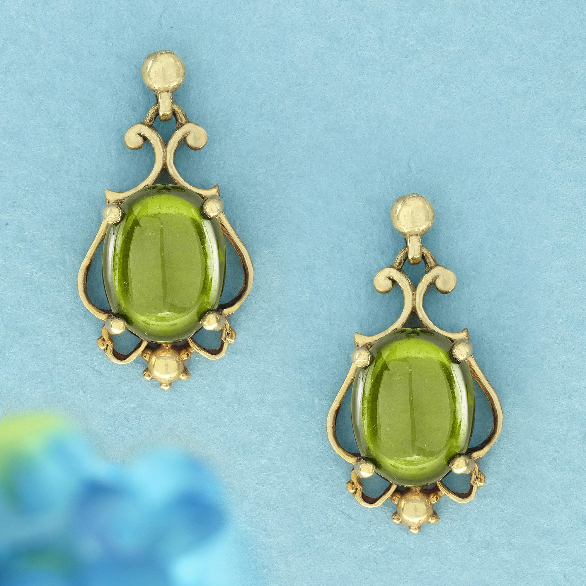 Feature captivating cabochon peridots that glow with a vibrant green hue, suspended in an elegant, vintage-inspired setting. The overall design resembles a magical lantern or lamp, with the smooth, oval shape of the peridots reflecting light in a
