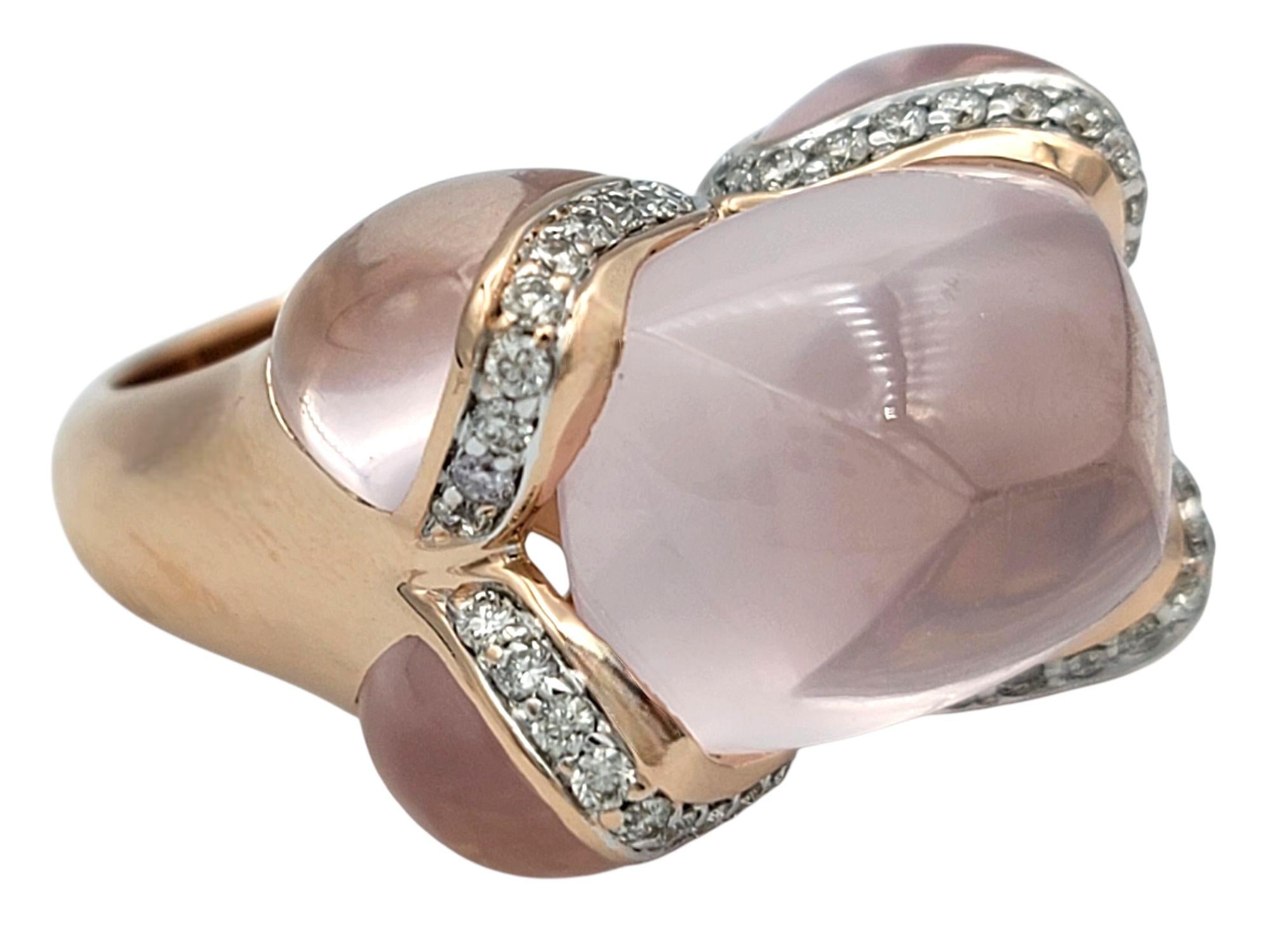 Ring Size: 7

This enchanting ring showcases a luminous cabochon-cut rose quartz at its center, exuding a soft blush hue that feels both romantic and serene. The rose quartz is embraced by flowing ribbon-like accents adorned with sparkling pave