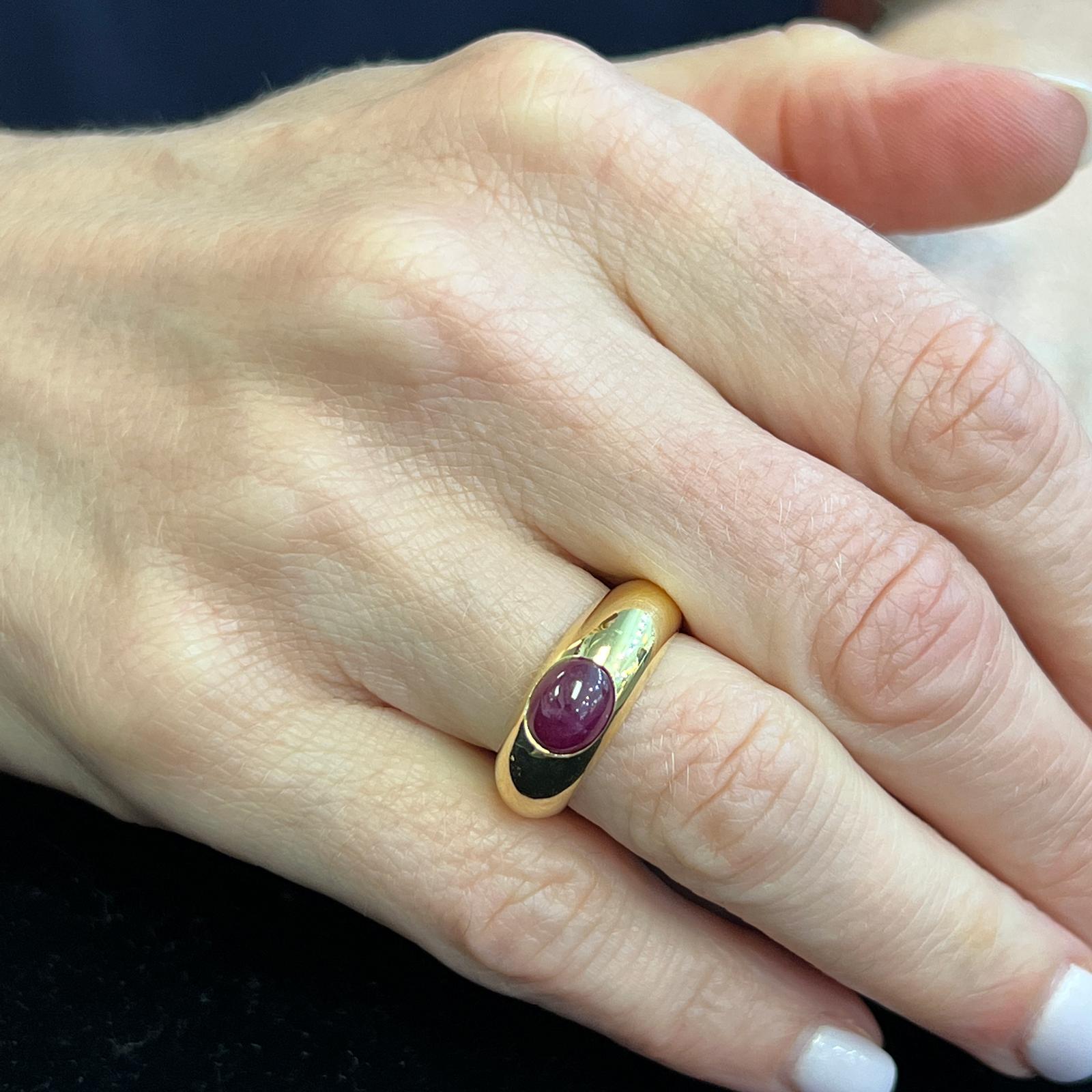 Cabochon ruby band ring handcrafted in 18 karat yellow gold. The ring features a natural ruby gemstone weighing approximately 1.50 carats. The bezel set ruby is set in a contemporary rounded gold band measuring 7.6mm in width. The ring is currently