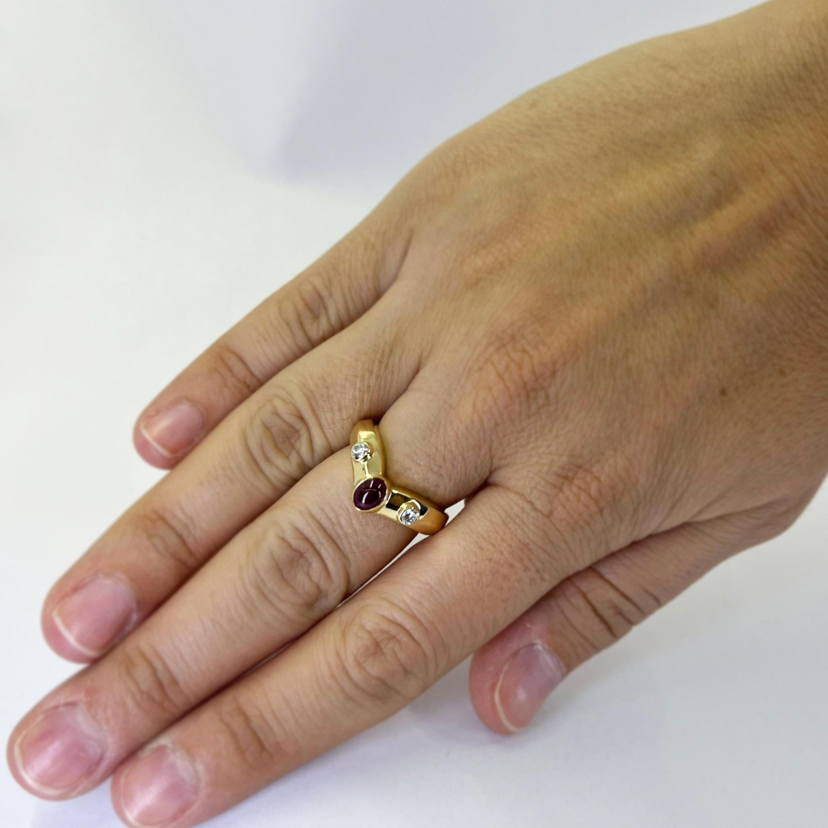 18 karat yellow gold contour band featuring a 5.5mm x 4mm cabochon ruby accented by 2 round brilliant cut diamonds of VS clarity and H color totaling 0.20 carats. Finger size 6.5. Includes One Sizing Service Upon Request, Prior to Shipping. Finished