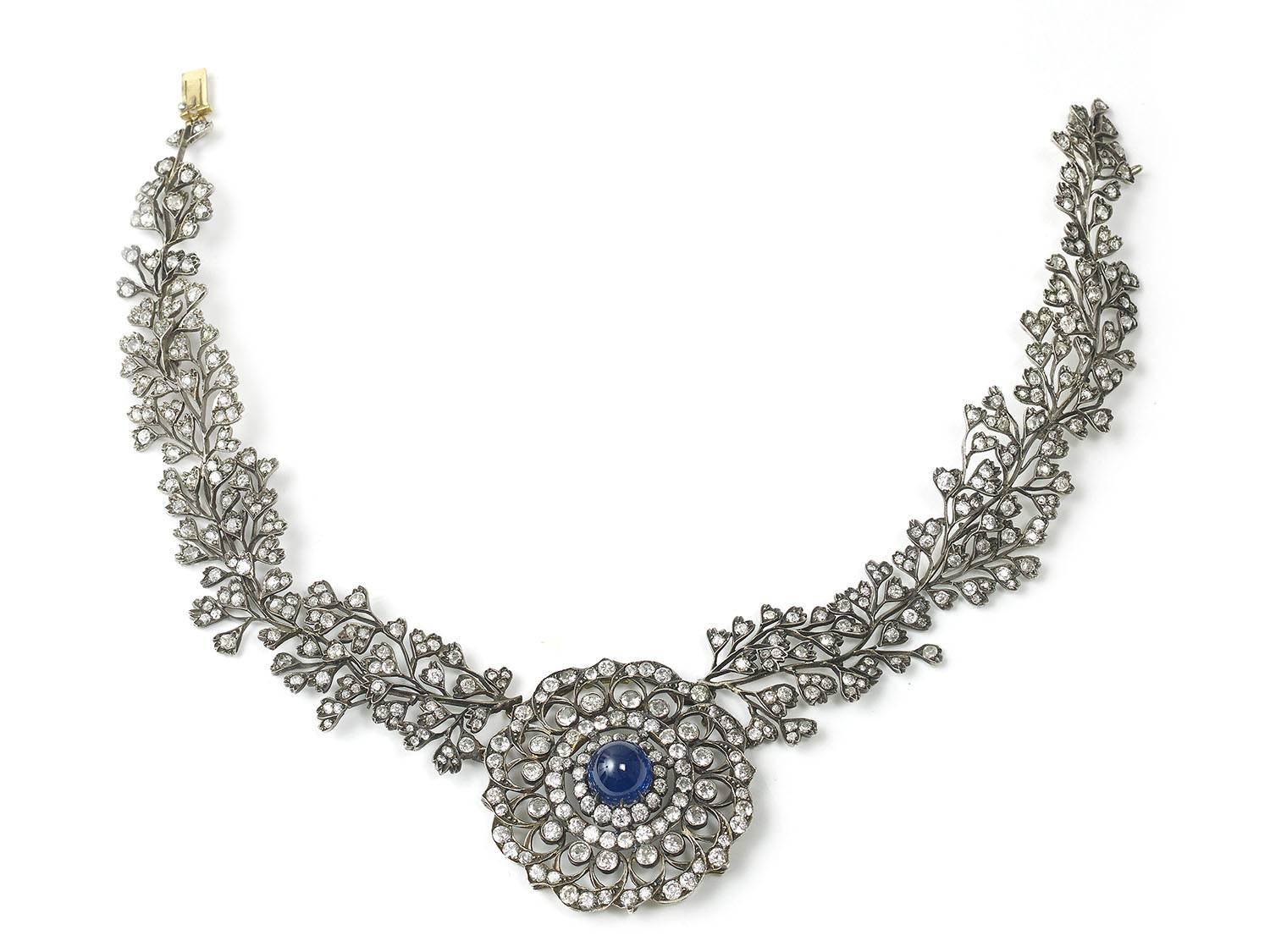 A sapphire and diamond necklace, central circular panel, set with a high cabochon-cut sapphire measuring approximately 12.34 x 12.56mm, within a floral openwork design of old-cut diamonds, integrated collar featuring branches, set with old-cut