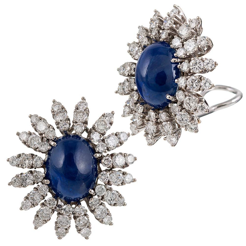 Glamourous high jewelry from the mid-20th century, the earrings are made of 14 karat white gold and set with a pair of cabochon sapphires which weigh approximately 20 carats in total. The center stones are encircled by bursts of brilliant white