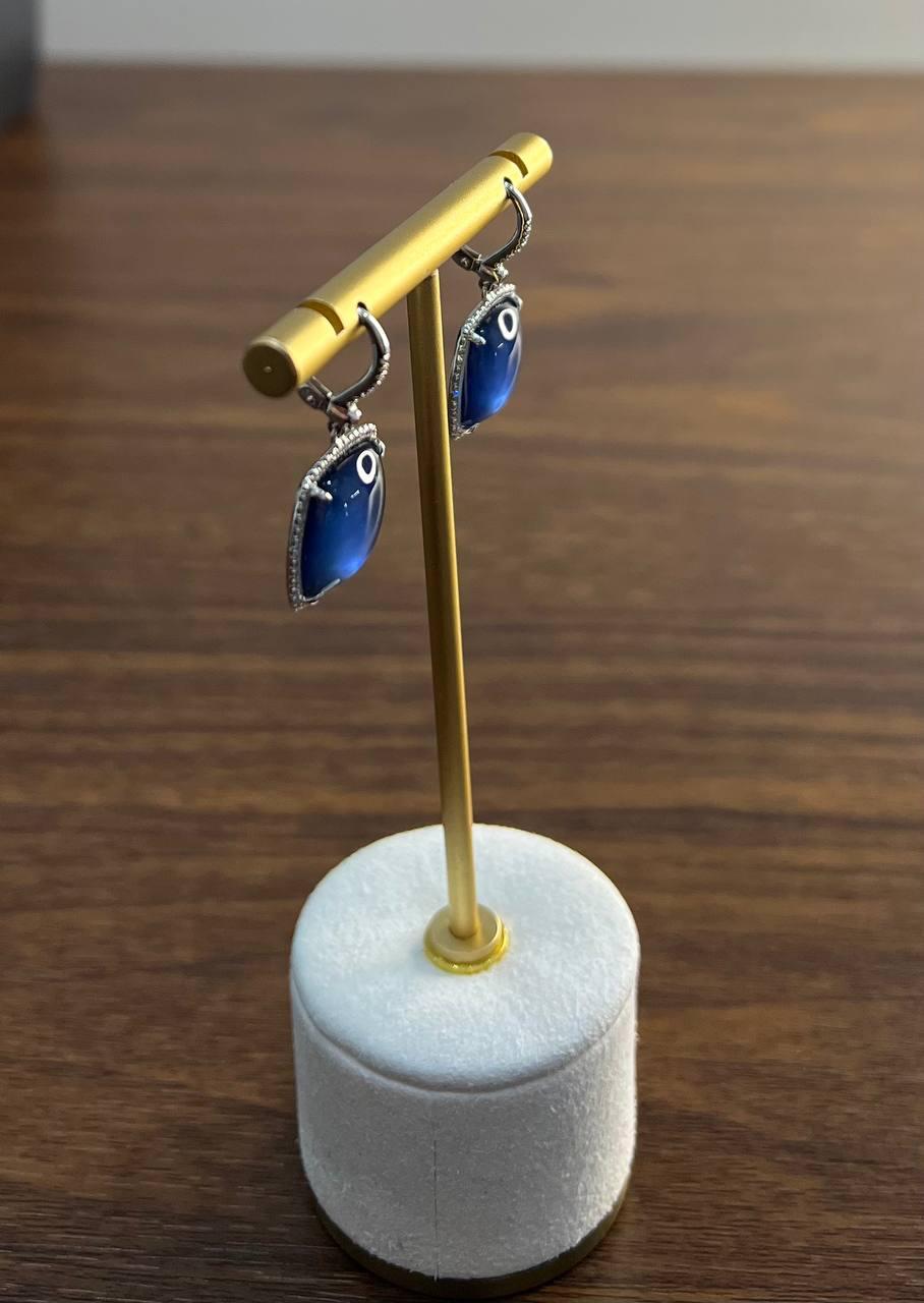 Elegant tourmaline and diamond drop earrings: these sophisticated earrings are crafted in 14K white gold.

Each earring features a blue tourmaline indicolite cabochon, set within a delicate white gold halo of diamonds.

The bezel is adorned with