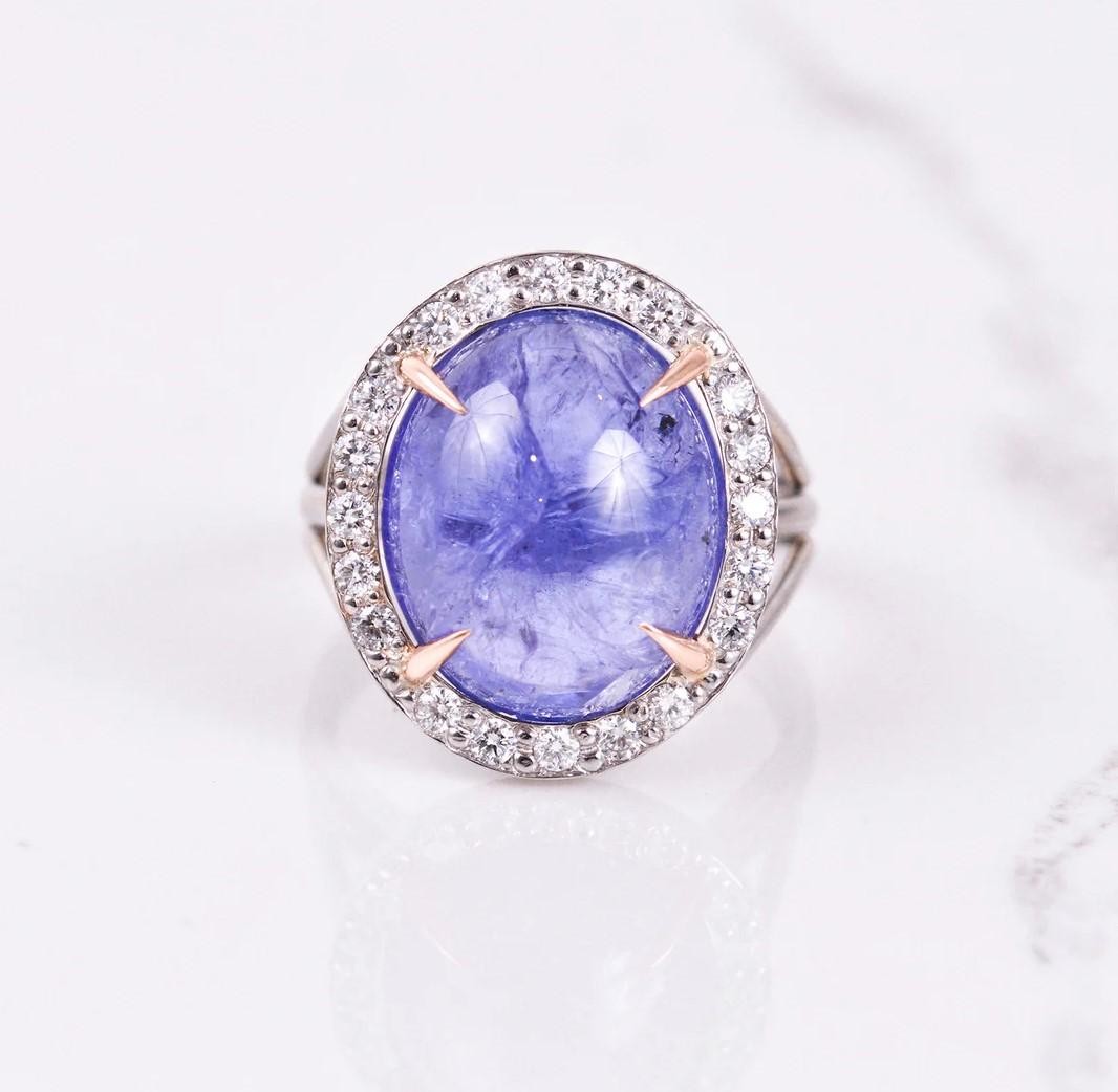 This hand fabricated ring is quite extraordinary! In the center is a 14.81 carat cabochon cut tanzanite surrounded by a .43 carat diamond halo, set in 14k white gold with 14k rose gold prongs. Ring size is a 7.
