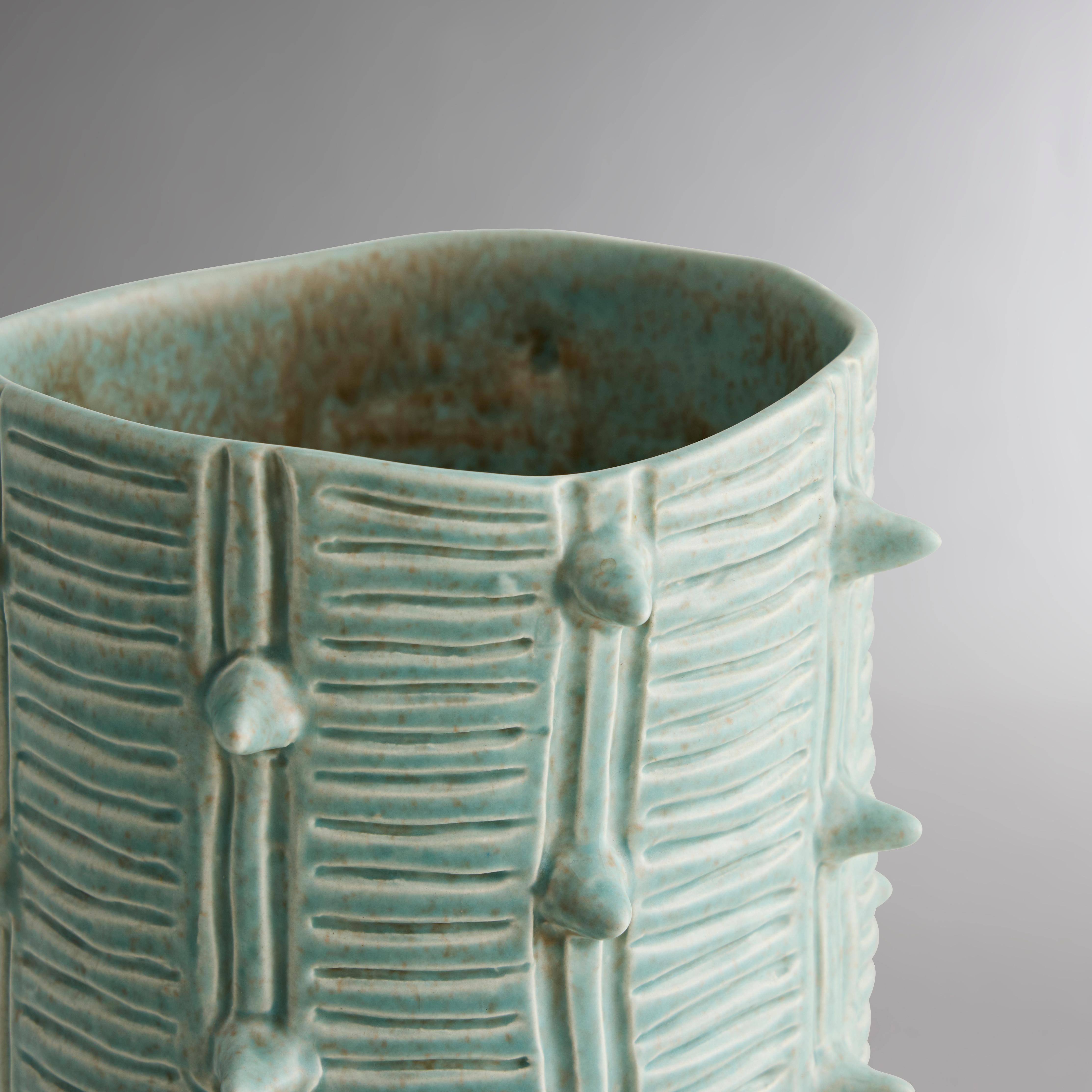 Fabriqué à la main en argile naturelle, ce vase organique adopte le charme d'une succulente du désert avec des gravures géométriques et de petites pointes. La glaçure aigue-marine laisse entrevoir la forme de la faïence fauve du vase CACTI dans