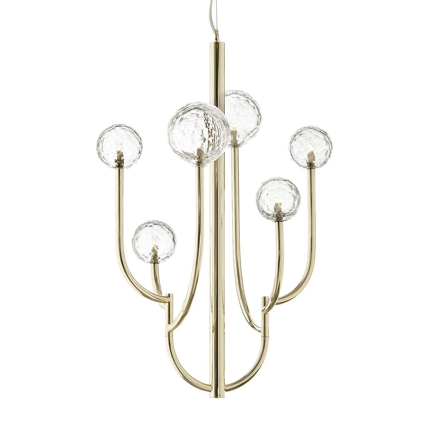 Sophistiqué et unique, ce lustre présente une structure métallique minimaliste avec une finition dorée douce mettant en valeur six globes de cristal italien taillé à la main et disposés à différentes hauteurs. Montés sur un poteau central, les deux