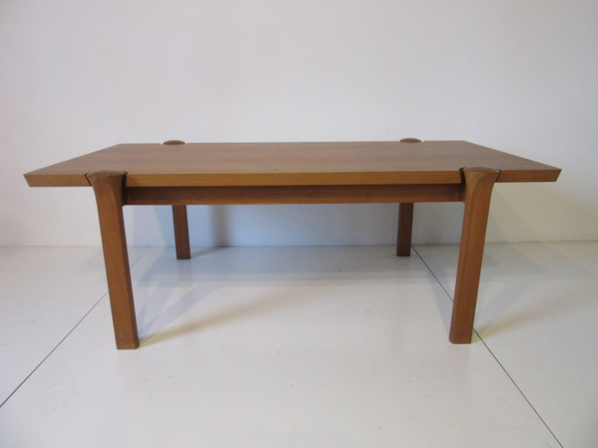 A teak wood Danish coffee table with great graining and surface cutouts exposing the top of the legs, well crafted and heavy, retains the manufactures tag to the bottom side. Manufactured in Denmark by Cado Mobler.