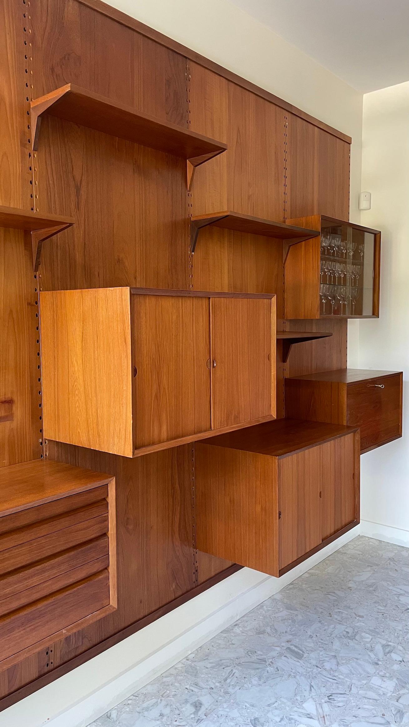 Scandinavian wall system by Poul Cadovius from the 1960s, made of teak, composed of four panels supporting several shelves and adaptable cases:

- 3 shelves 
- 2 boxes with sliding doors
- 1 glass sliding door cabinet 
- 1 pedestal with 3