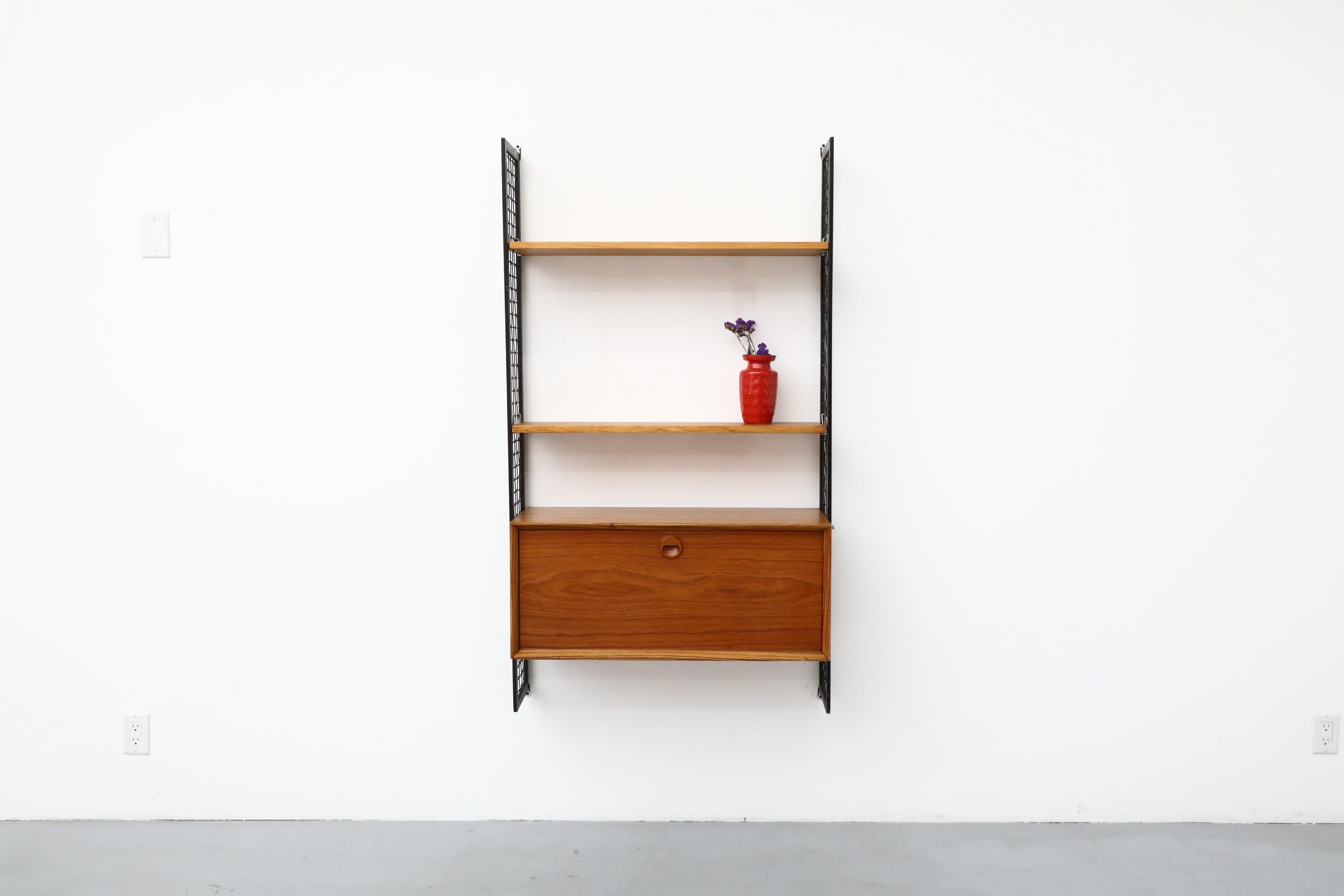 Mid-Century Zebrawood, Teak, Elm, and Laminate wall unit with two shelves and drop down cabinet mounted on black enameled metal grid risers. This unit is completely adjustable. In original condition with visible wear consistent with its age and use.