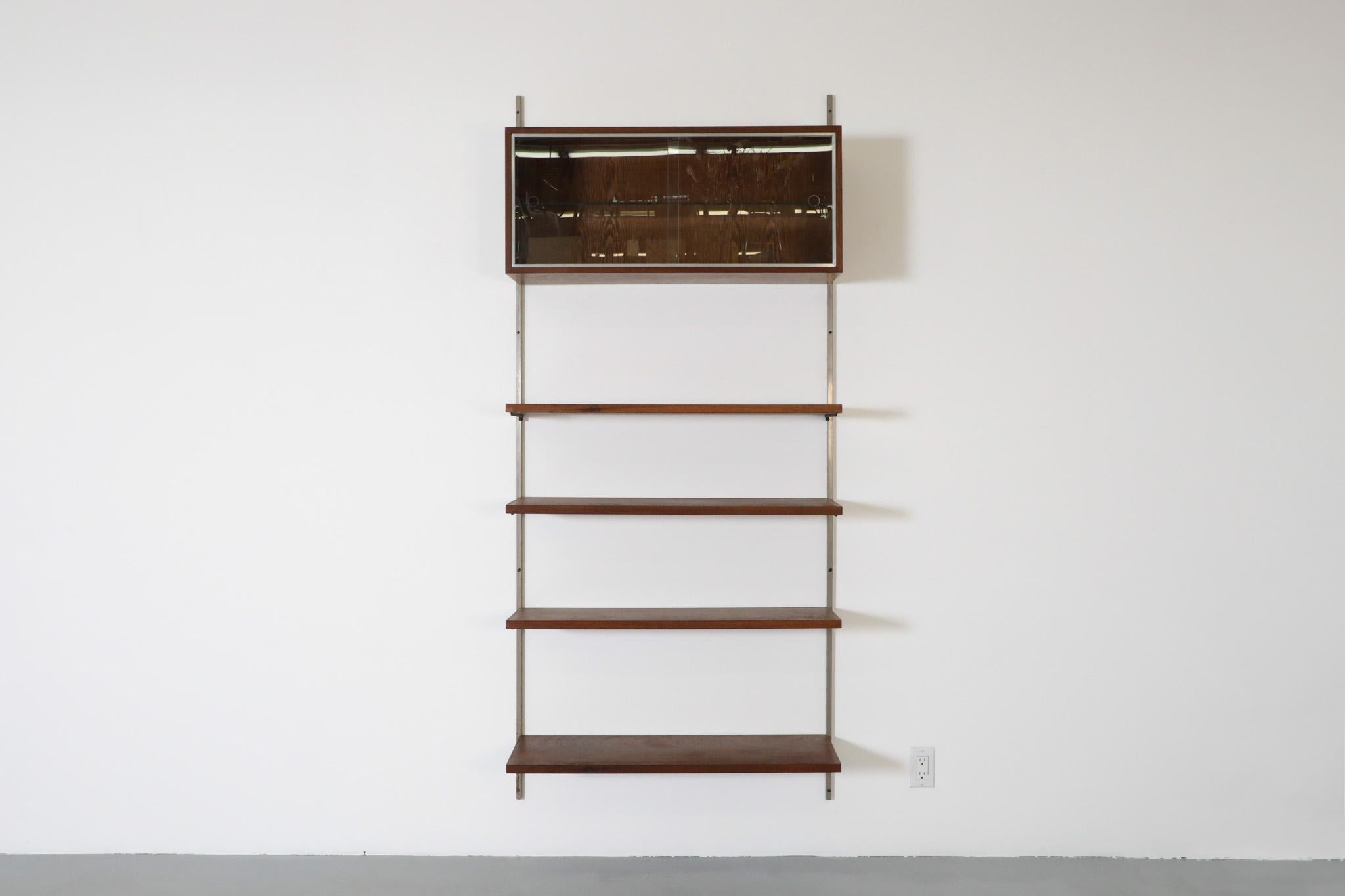 This Mid-Century wenge wall-mounted shelving system in the style of Danish designer Poul Cadovius has interchangeable shelves and a cabinet mounted on metal risers. The cabinet has newly made glass doors with circle cut-out handles and one inner