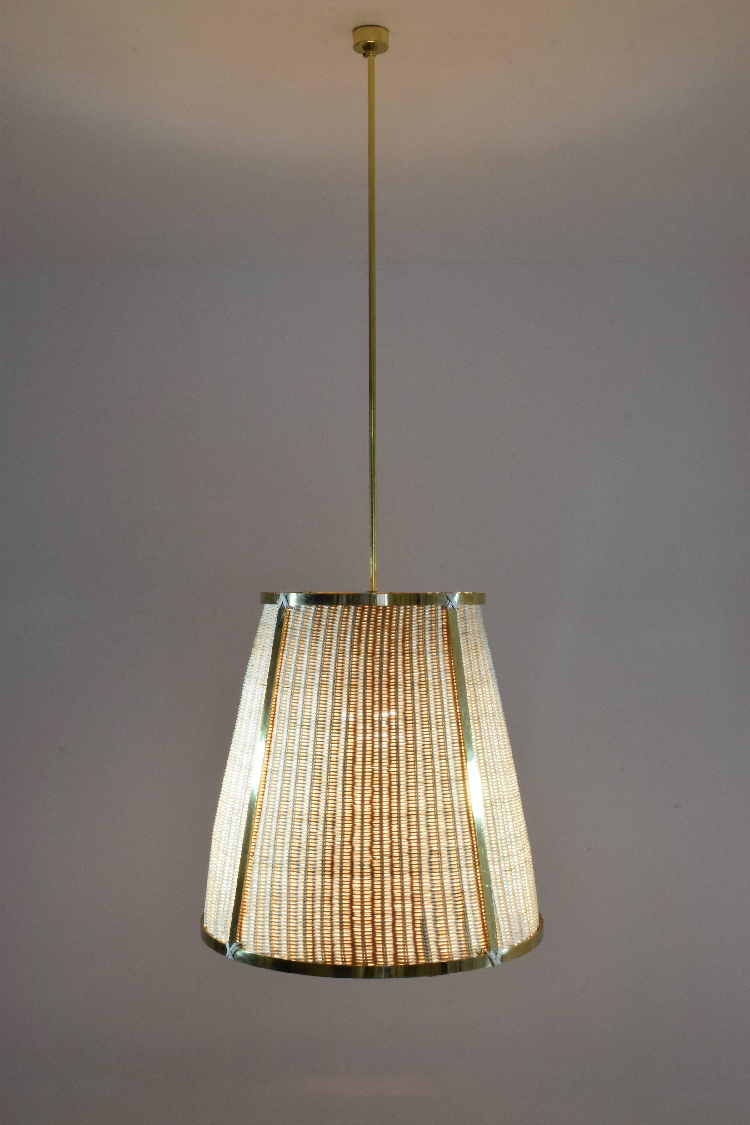 Le luminaire suspendu contemporain sur mesure Caeli-S est doté d'une structure en laiton fabriquée à la main par des experts et d'un abat-jour en rotin tressé à la main. Cette pièce crée une ambiance chaleureuse et accueillante, parfaite pour les