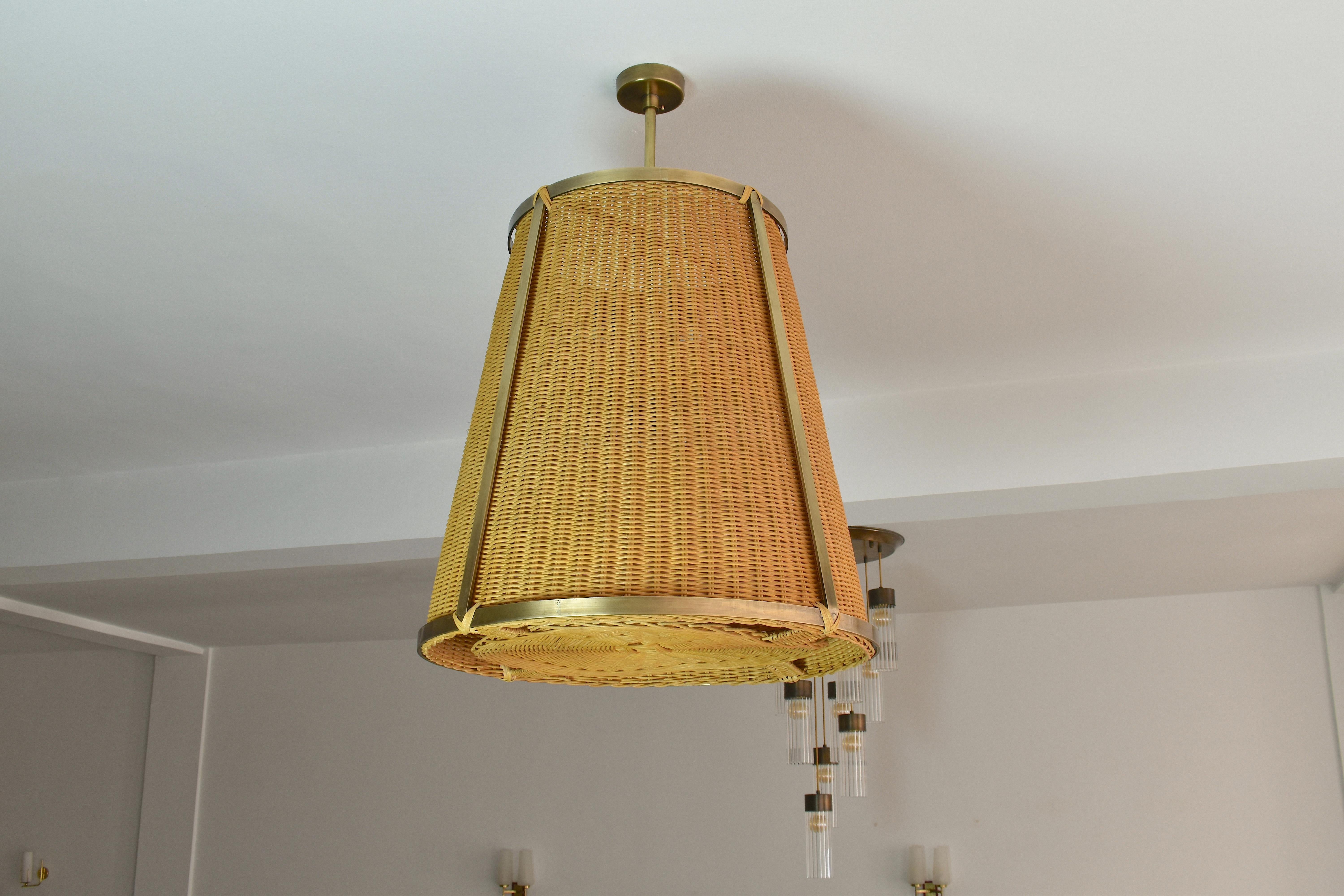 The Caeli-SD contemporary handcrafted made-to-measure pendant light fixture features an expertly handcrafted brass structure and a hand-woven dark-tinted rattan shade. This piece creates a warm and inviting ambiance, perfect for living areas or