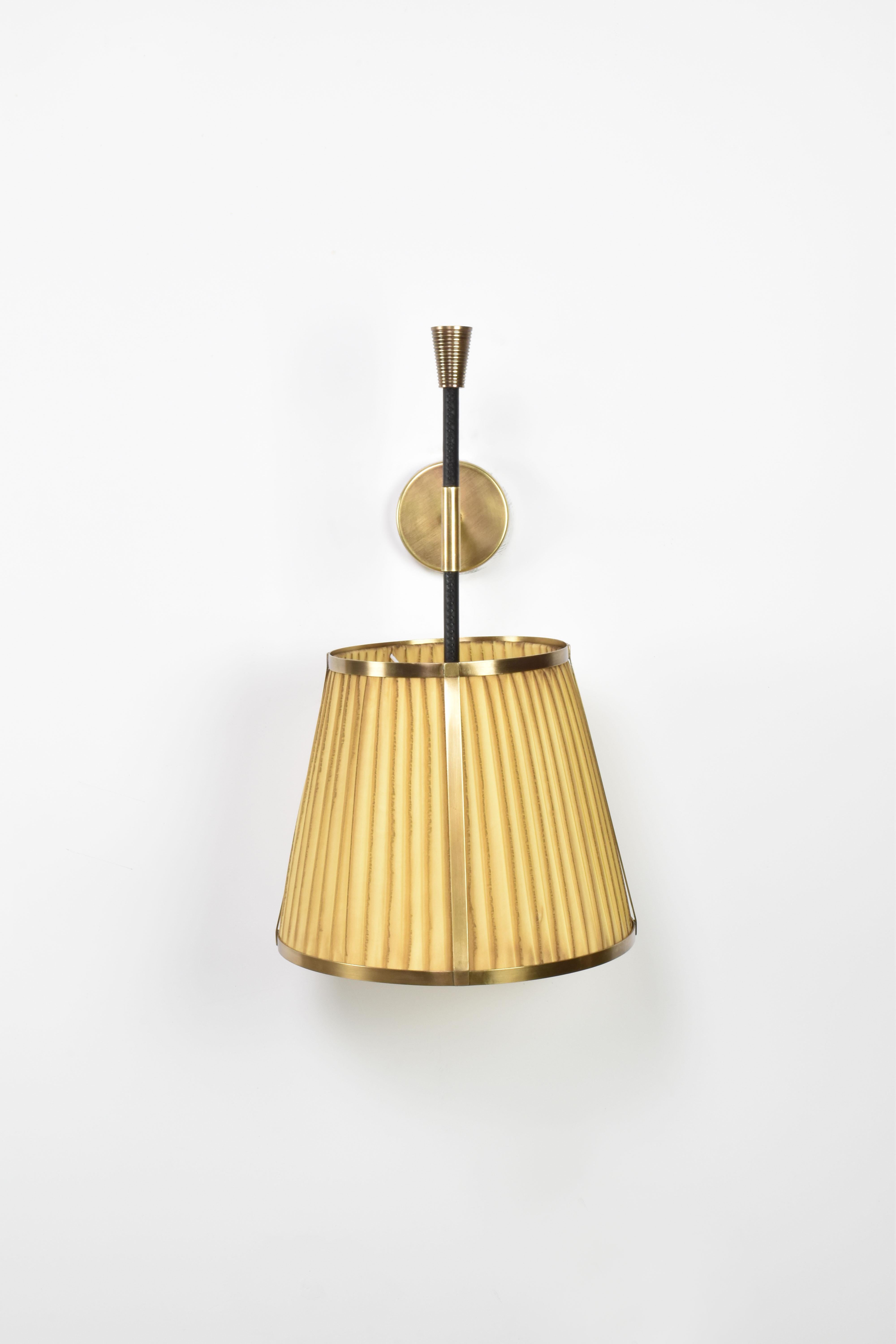 The handcrafted Caeli-w4 wall light, combines a modern brass structure with a unique, hand-dyed pleated fabric shade. The shade, available in either its natural state or a selection of dyed finishes, introduces subtle variations in each piece,