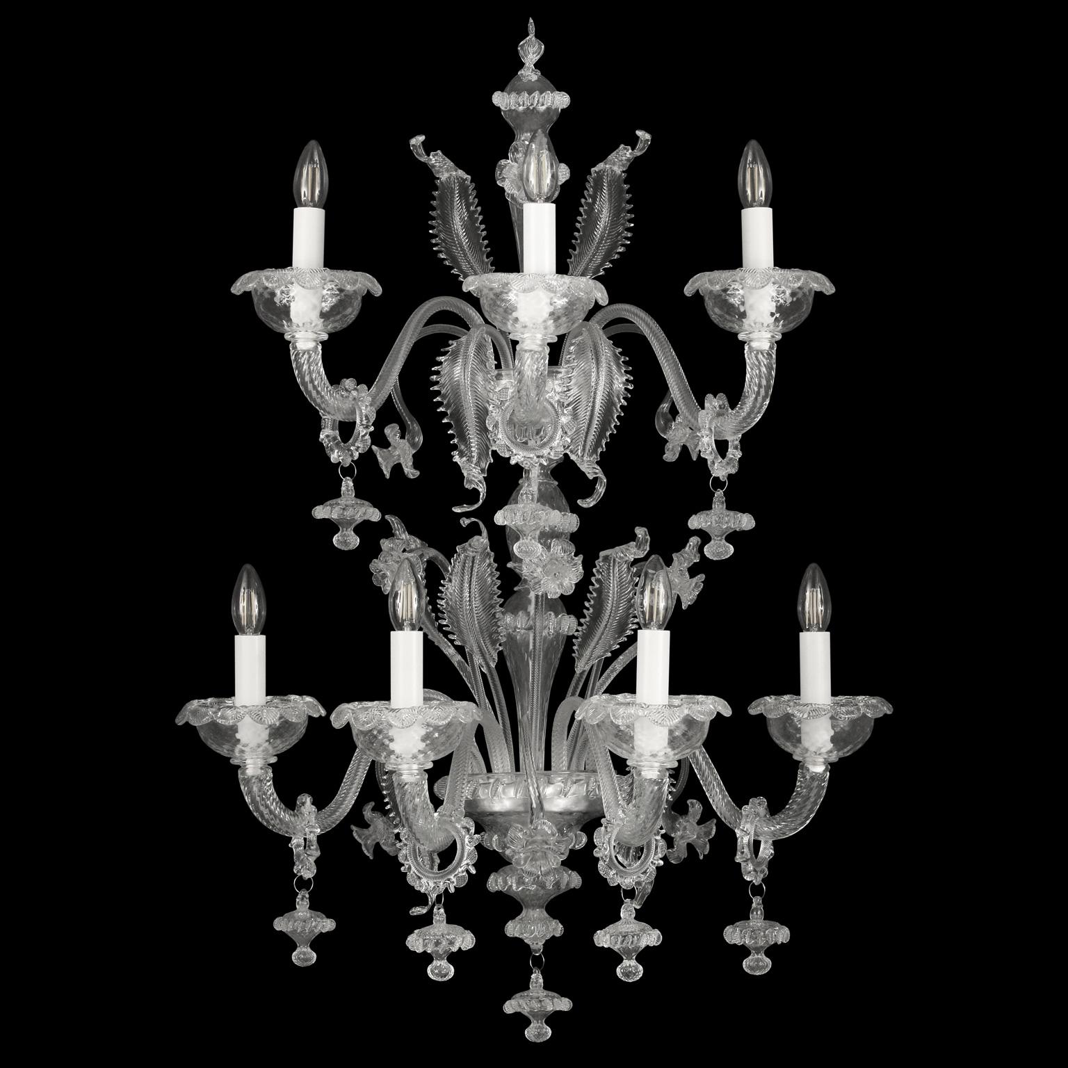 Caesar wall 4+3 lights, Venetian style, double tier in clear blown artistic glass by Multiforme
The name, as well as the structure evokes the splendour of the past centuries. It is an evergreen model, a classic product manufactured by our skilled