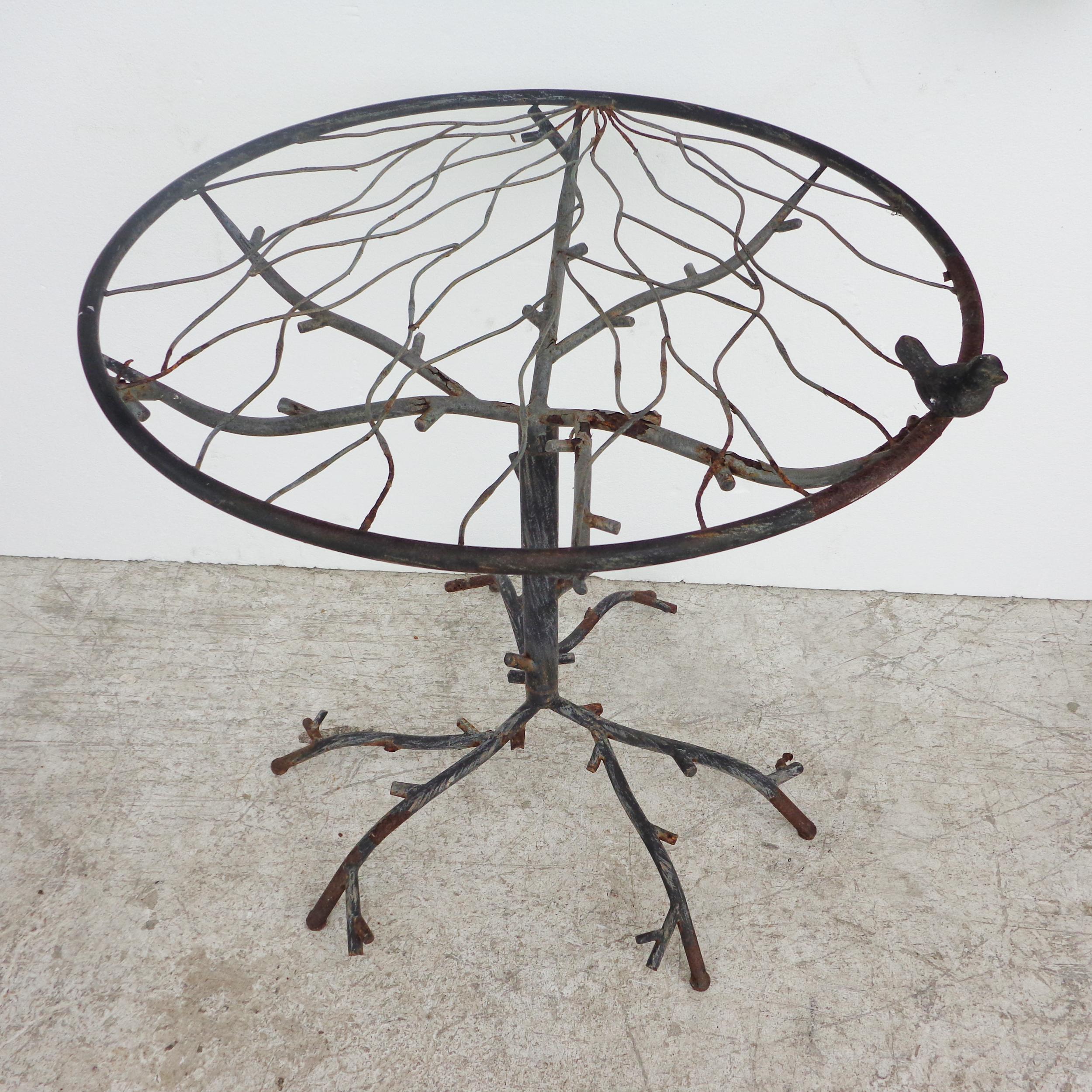 Cafe table in the manner of Diego Giacometti

Beautiful hand forged iron table with glass top 
Features carved tree branches under glass and at base with a small bird on the top.
 