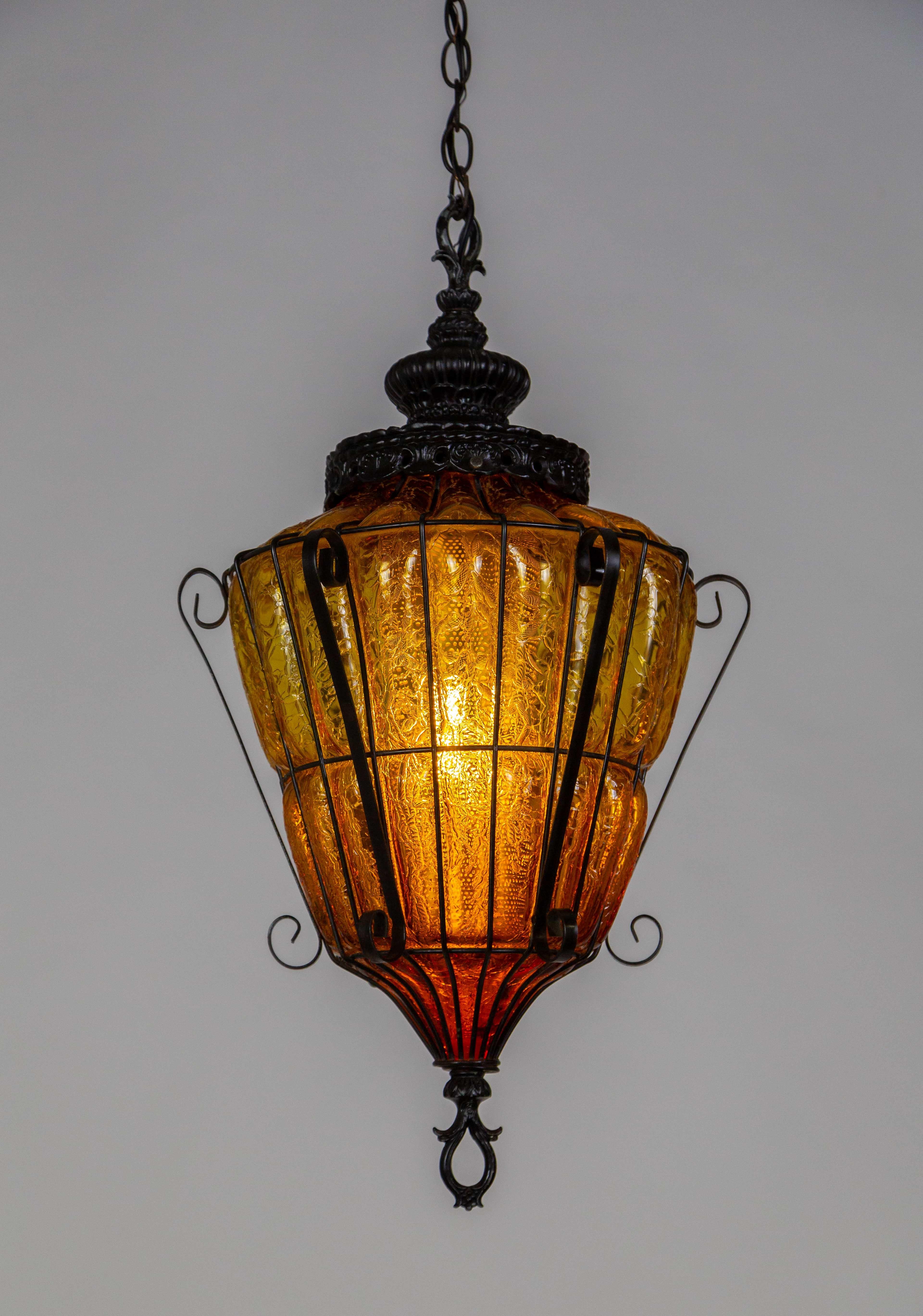 An amber, crackle, caged glass lantern pendant light from the mid 20th century; in an elegant shape with a decorative cap and s-curve accents. Newly rewired. 13