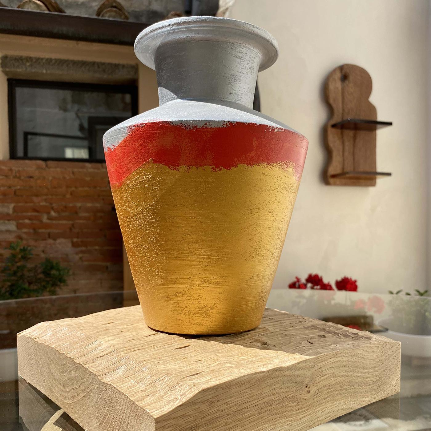 The Calafuria Cinque vase by Mascia Meccani is hand-turned and hand painted, bringing a rustic touch to any interior. Its biscuit terracotta silhouette is beautifully hand painted, boasting a gold base and gray top, and accented with a fiery red