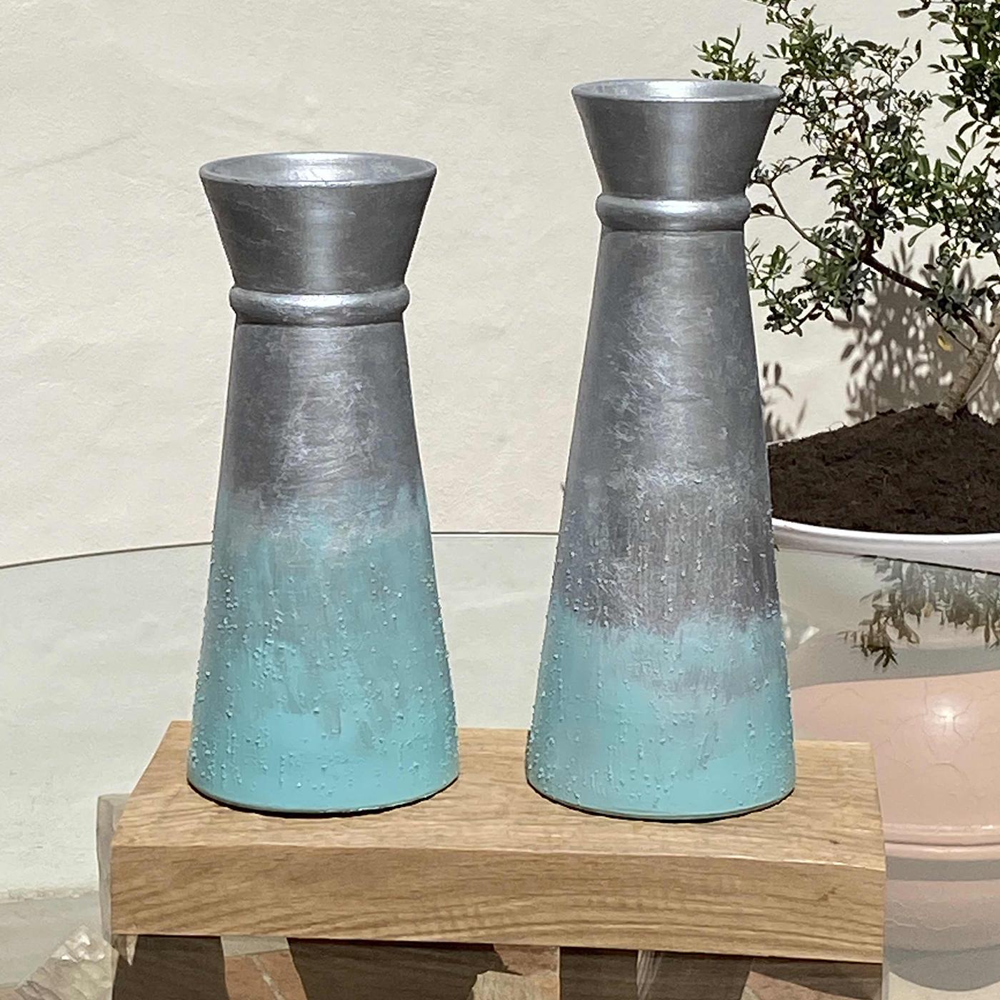 The Calafuria Due 2 vases by Mascia Meccani comprises two vases: one tall and one slightly shorter. Each hand-turned biscuit terracotta vase is hand-painted in sky blue and silver tones, enhanced with subtle textured detailing. Set on a sculpted