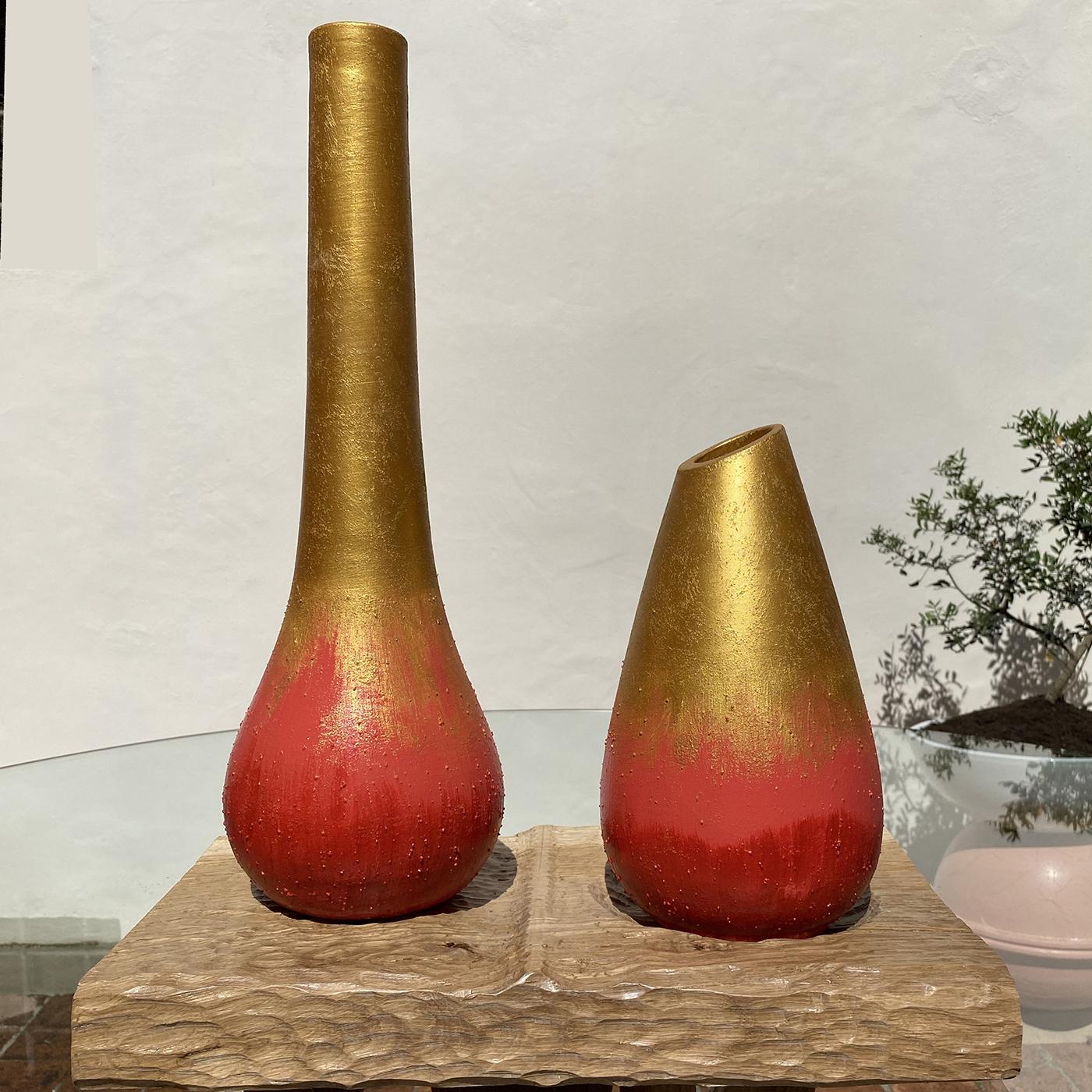 The Calafuria Uno 2 vases by Mascia Meccani comprises one tall vase with a slender neck and one shorter vase with a slanted top. Each item is hand-turned from biscuit terracotta, hand painted in red and gold. Set on a sculpted solid oak base for a