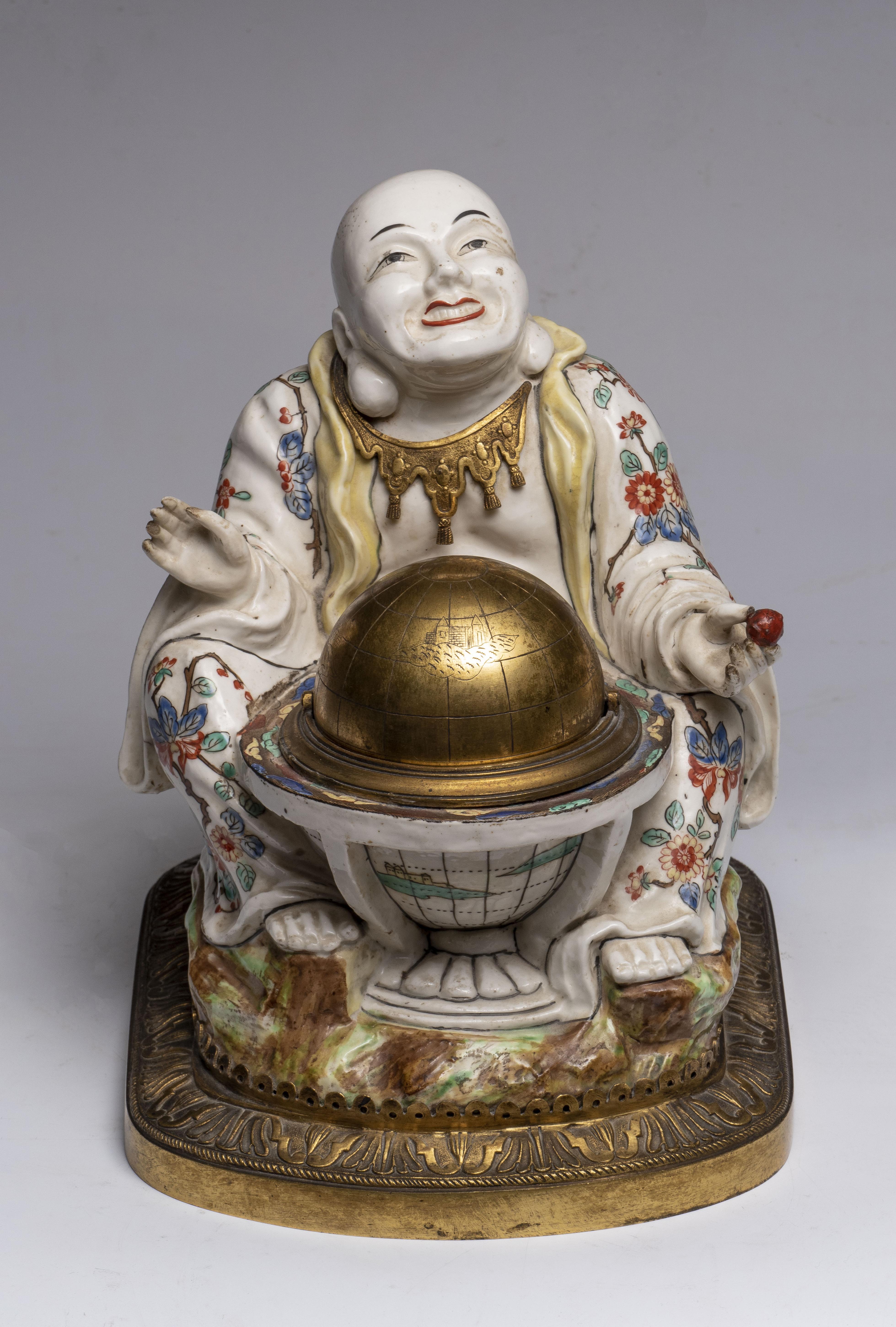 Das Objekt stellt einen sitzenden Buddha auf einem dekorativen Sockel dar, der ein kleines rotes Objekt hält. Die Buddha-Figur ist mit dem für die traditionelle Ikonographie typischen lächelnden, heiteren Ausdruck dargestellt. Der Buddha trägt ein